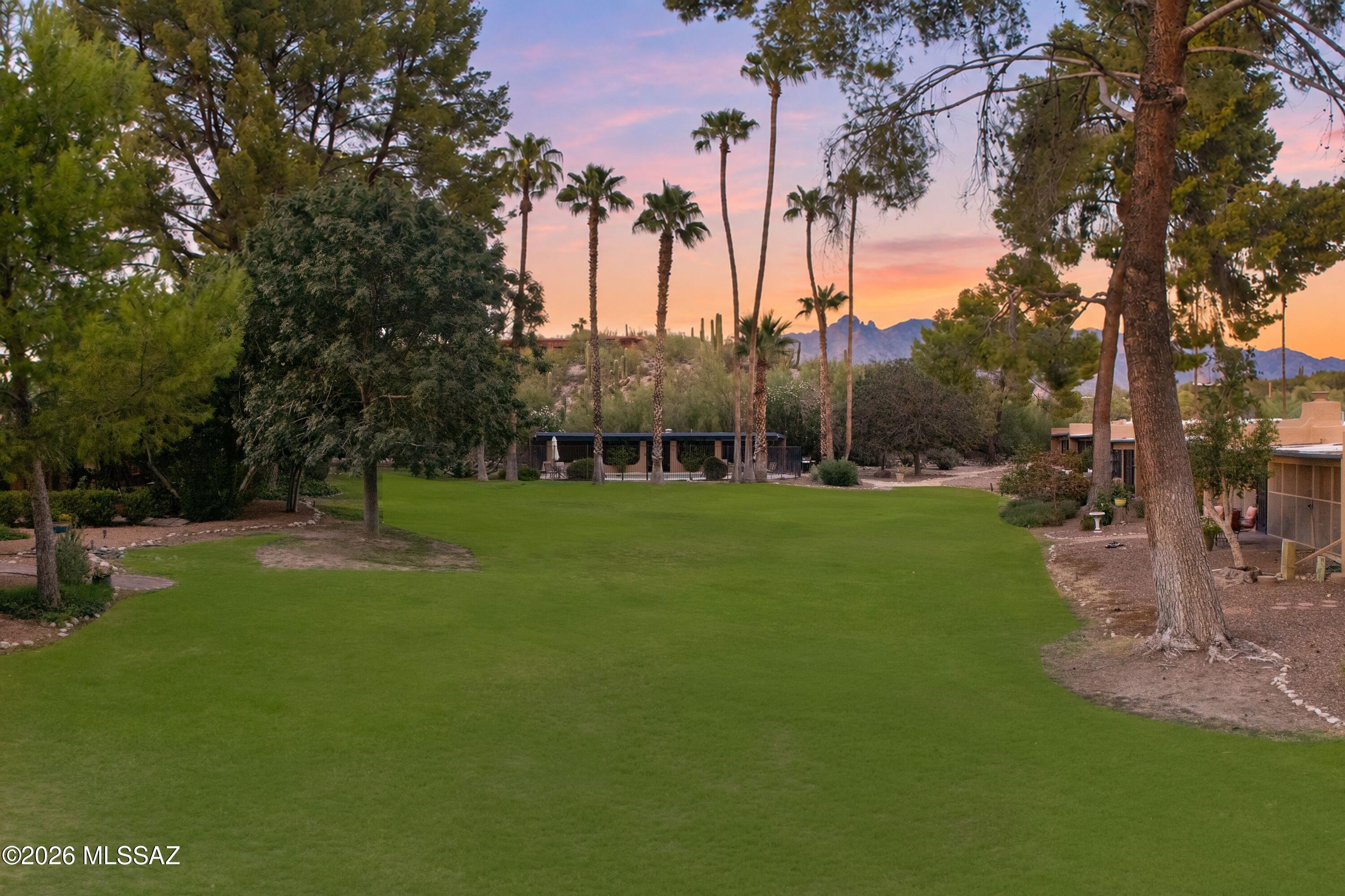 Expansive green lawn framed by palm trees, with distant mountains beneath a colorful dusk sky.
