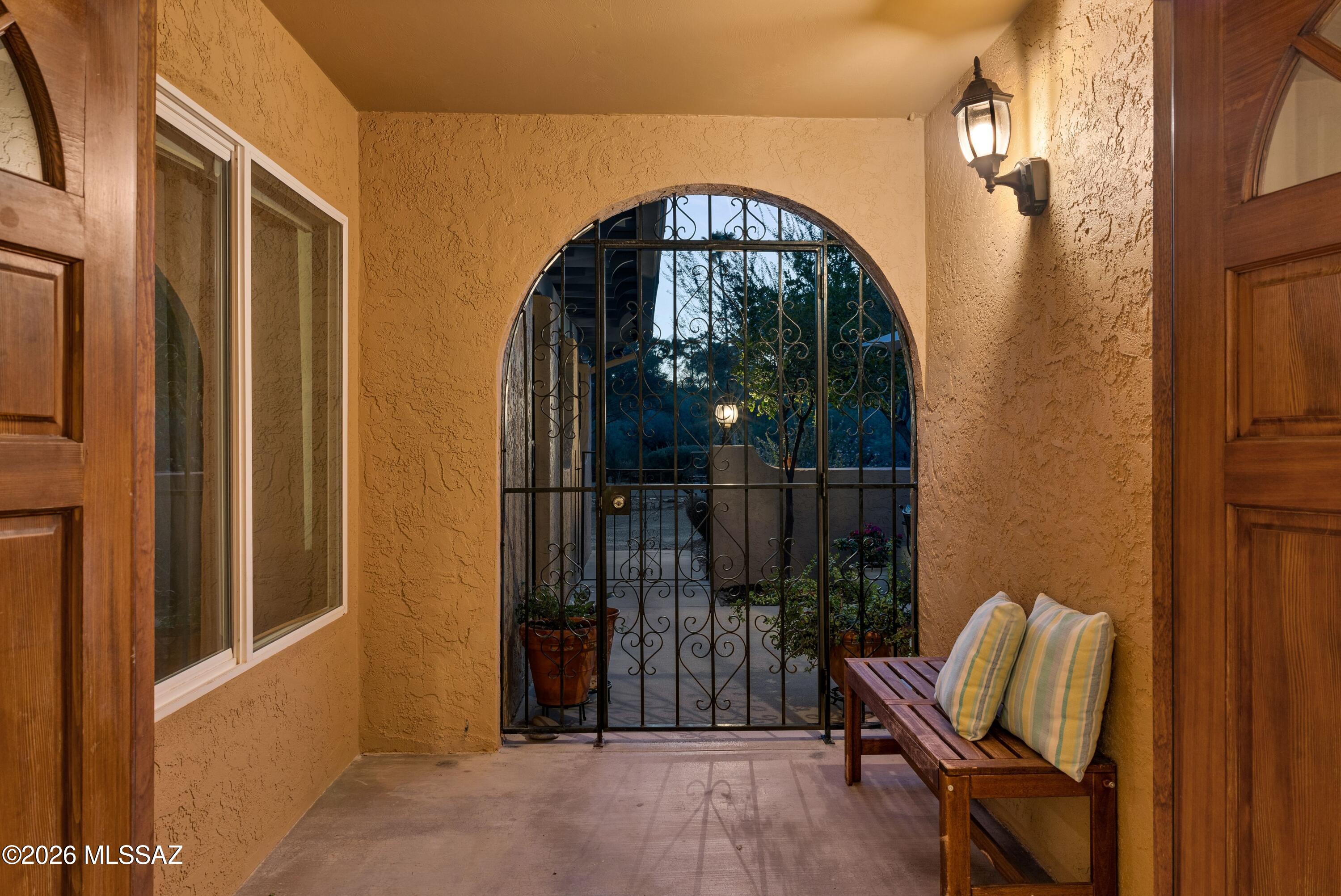 Covered entry porch with an arched wrought-iron gate and a wooden bench with striped cushions.