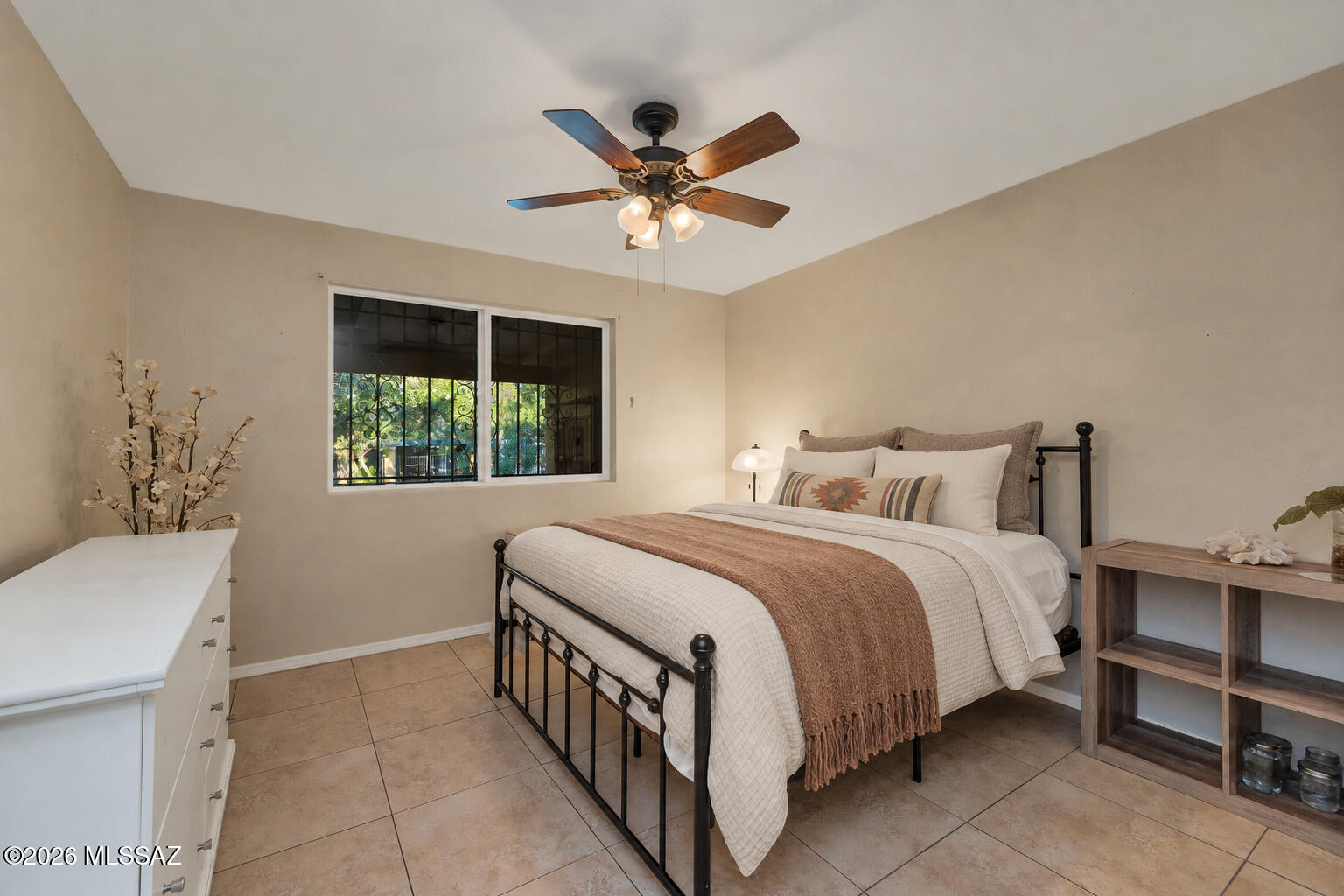 Bedroom with a black metal bed, rust-colored throw, wood-blade ceiling fan, and barred window.