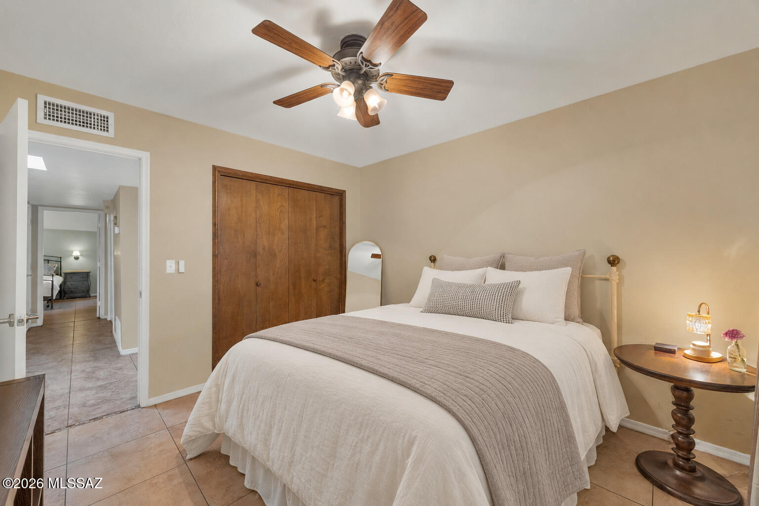 Bedroom with a white bed, wood closet doors, ceiling fan, and open doorway to another bedroom.