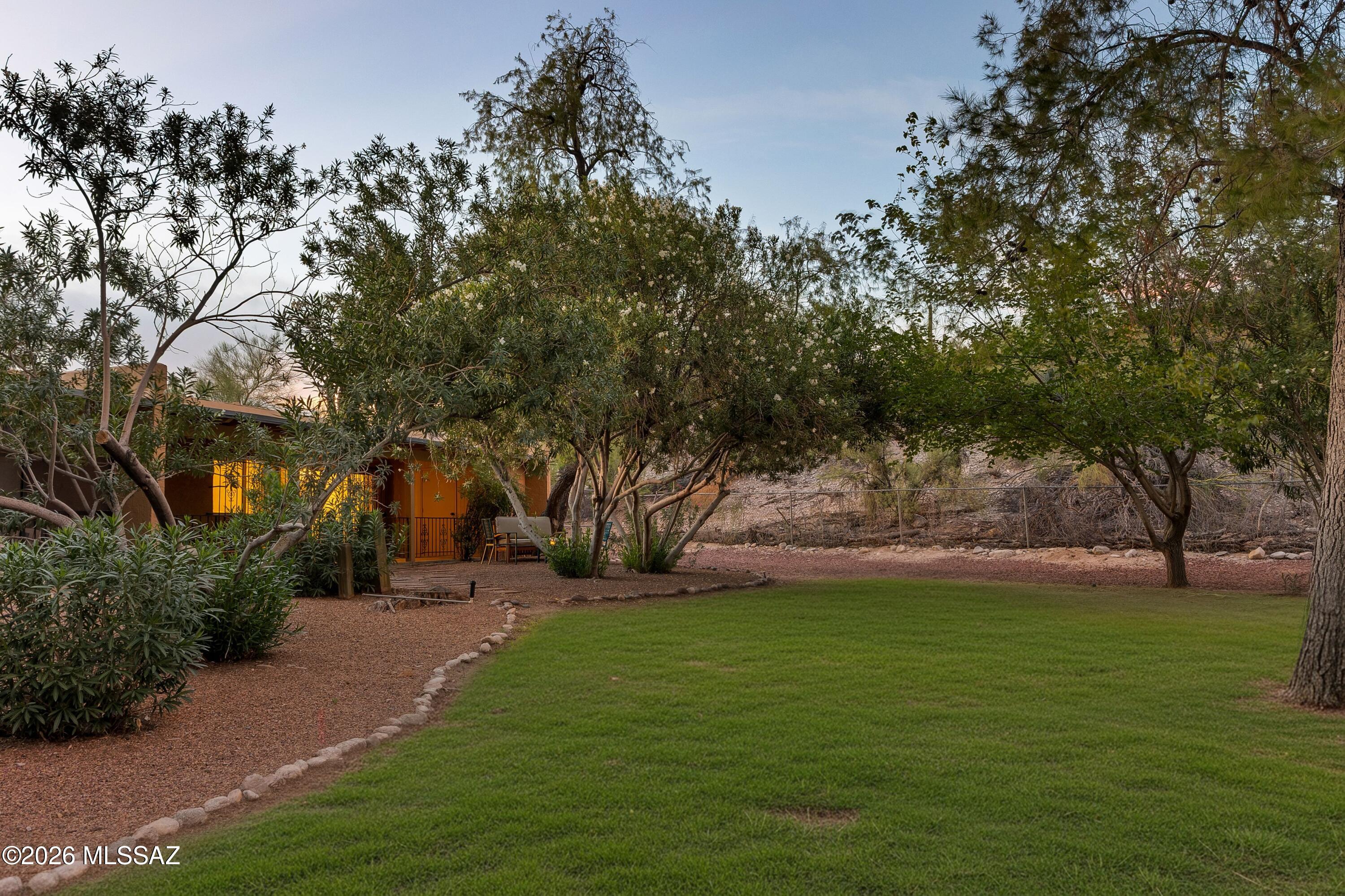 Backyard with a green lawn, mature trees, gravel paths, and patio seating beside the home.