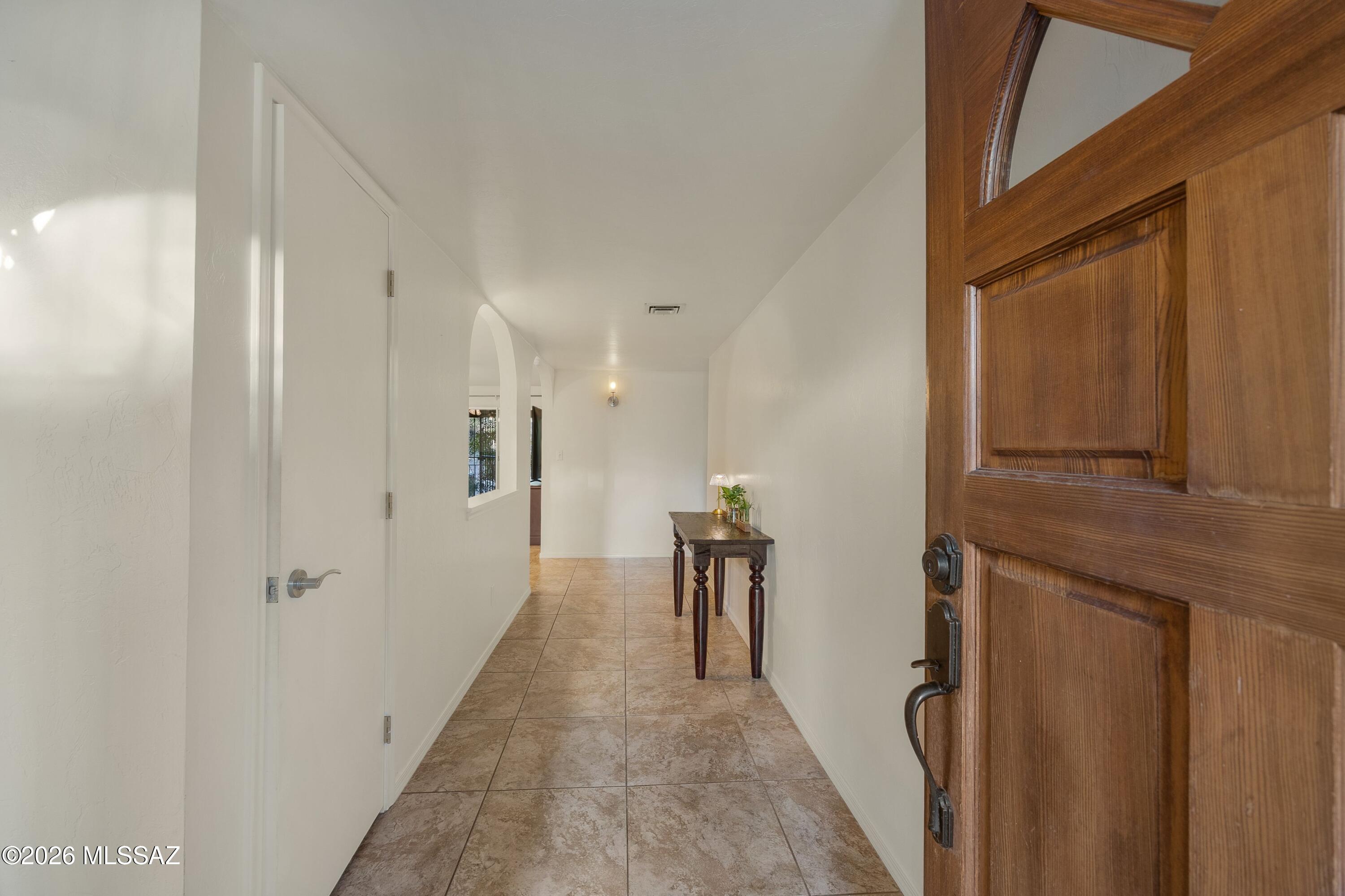 Entry hallway with tan tile floors, a paneled wood front door, and a console table.
