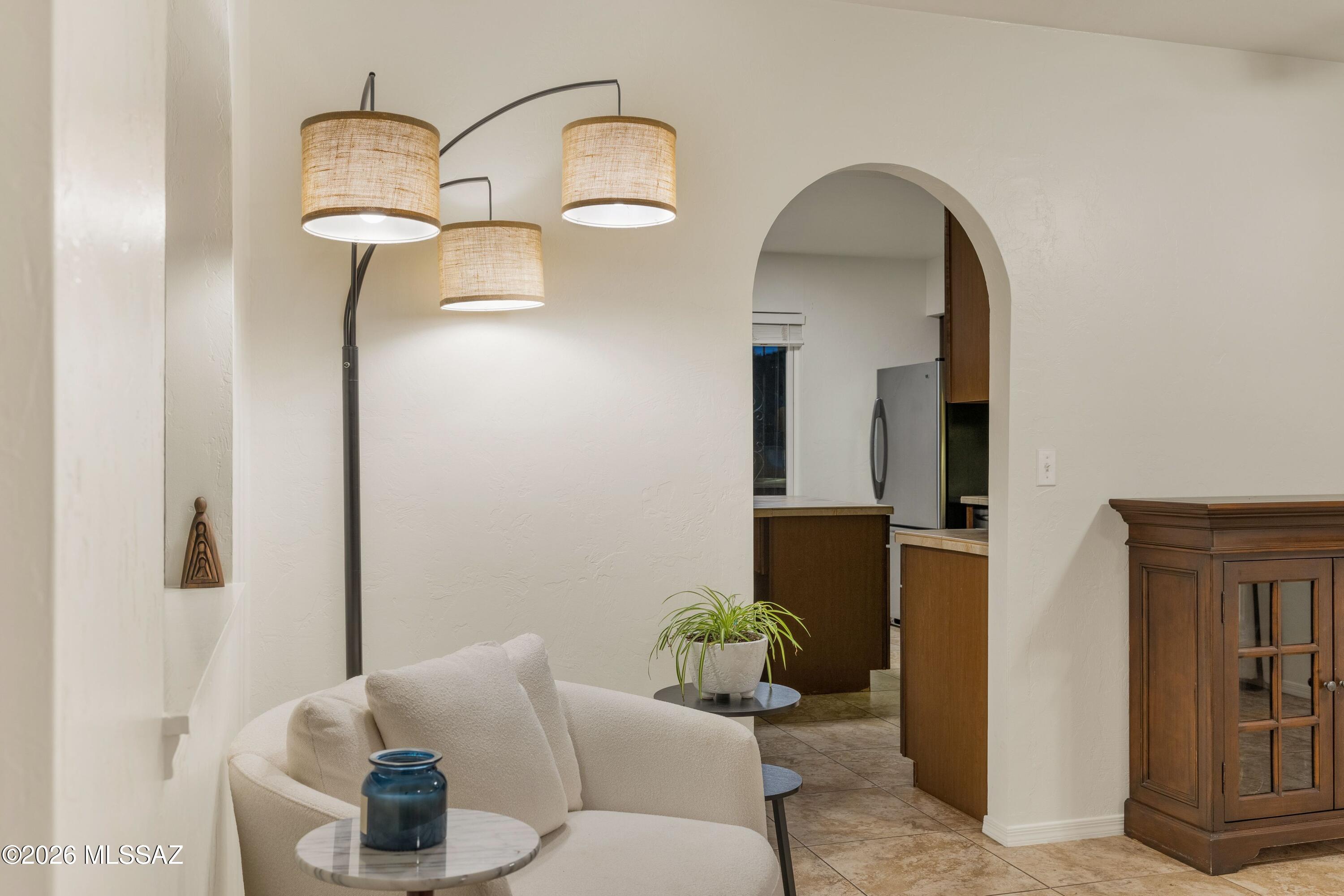 Furnished living room with a cream sofa and arched opening to a wood-cabinet kitchen.
