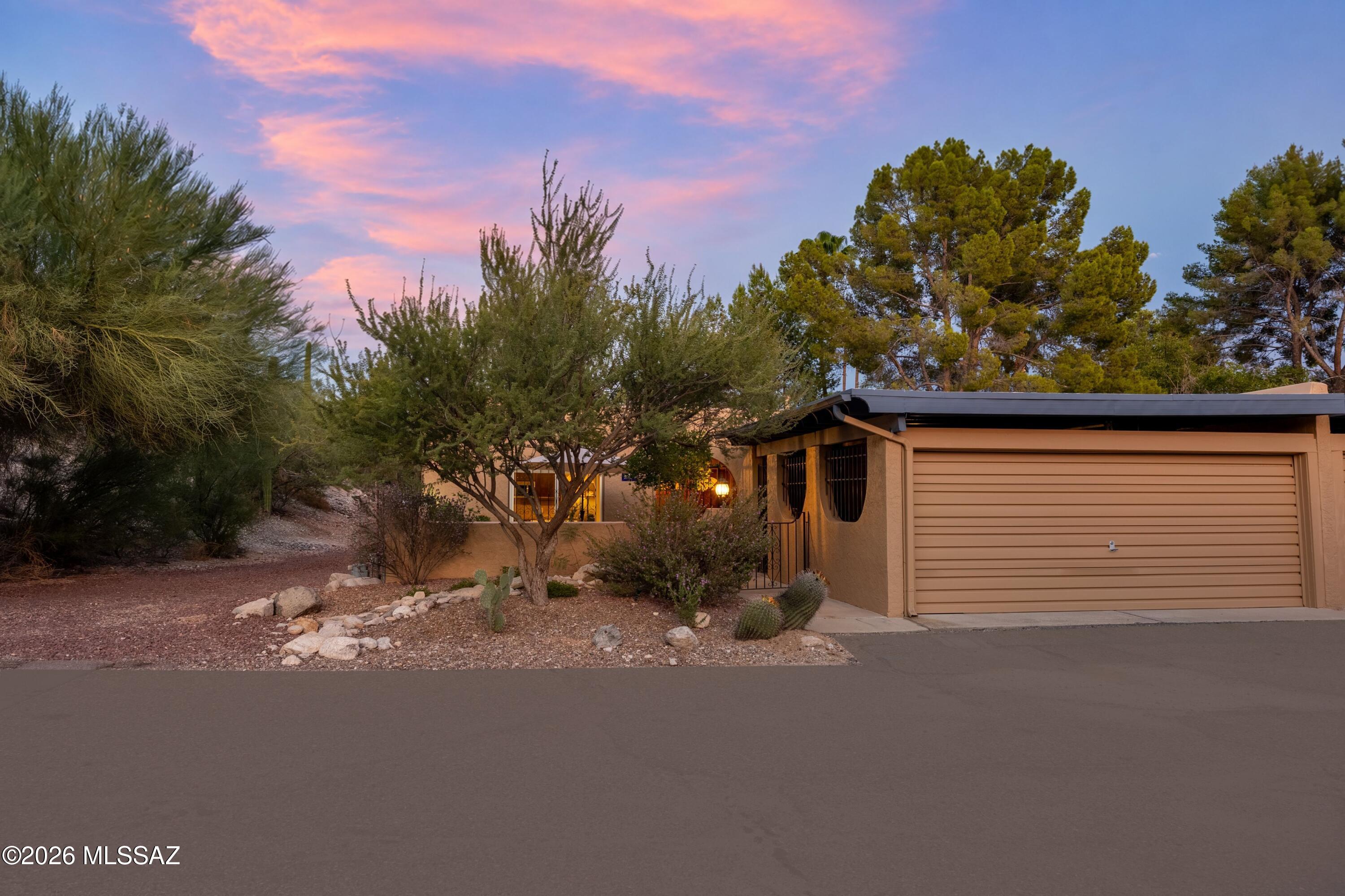 Tan home with a two-car garage and desert landscaping beneath a pink dusk sky.