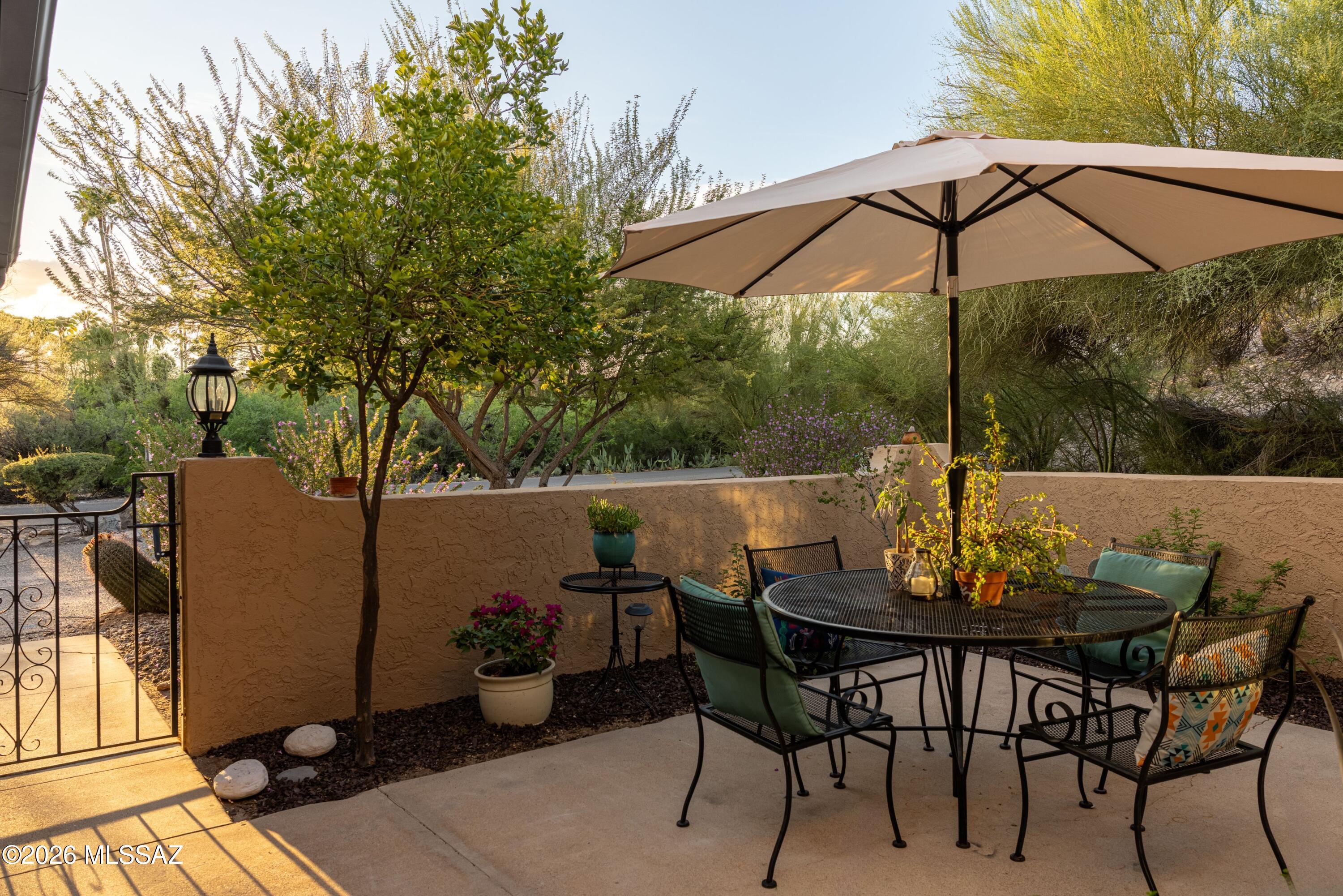 Outdoor patio with a shaded dining table, cushioned chairs, and desert landscaping.
