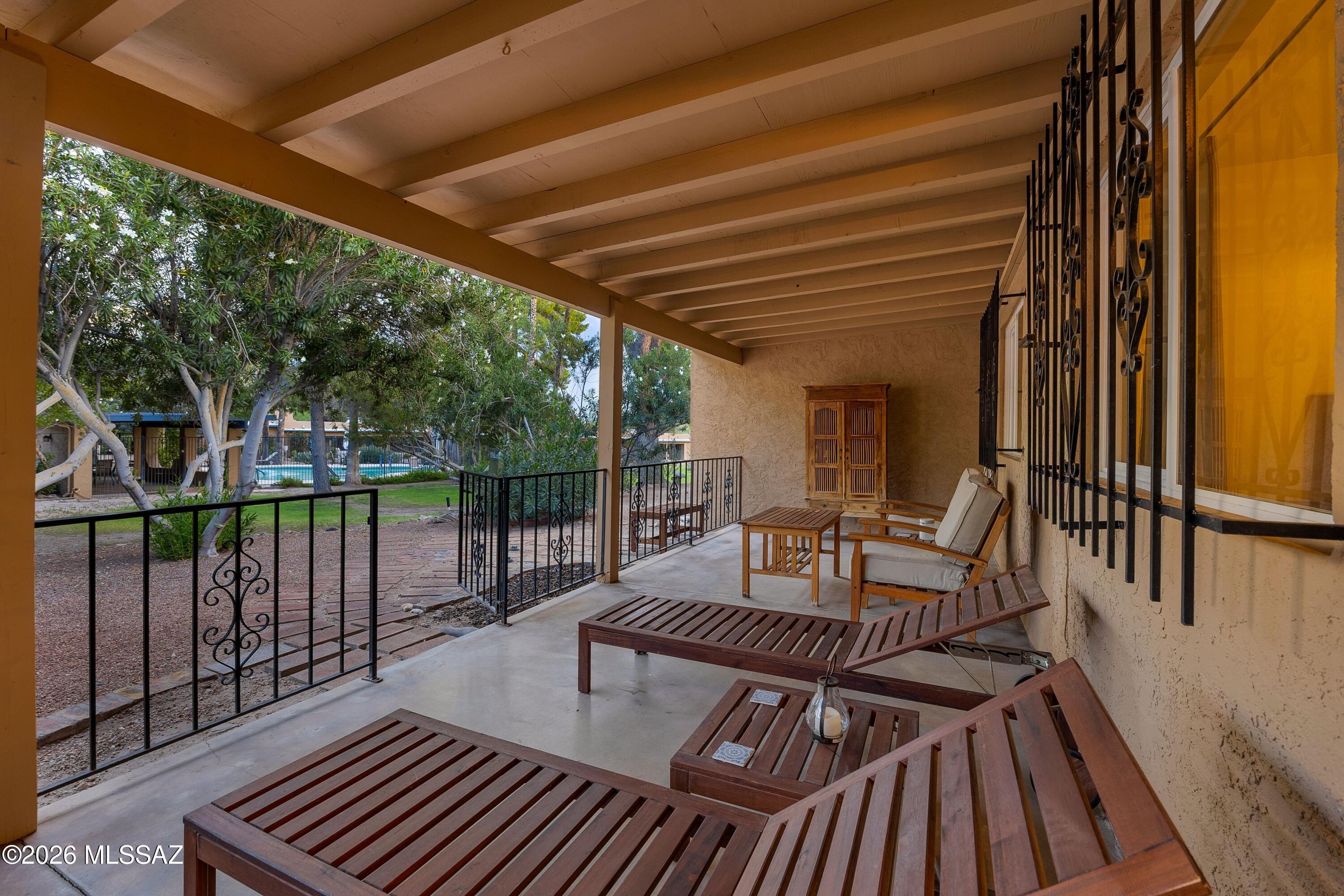 Covered patio with wooden lounge furniture and views of trees and a swimming pool