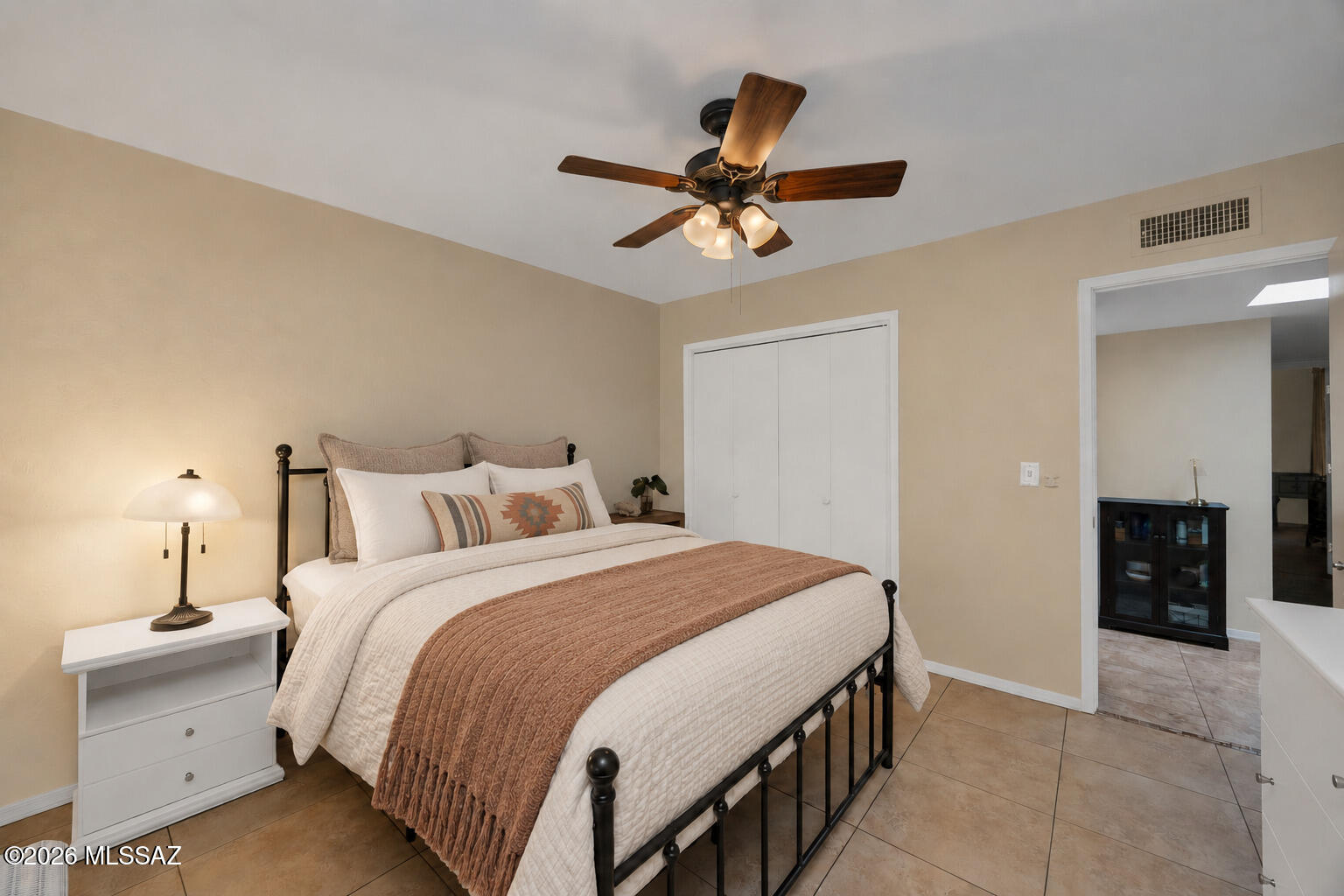 Bedroom with a black metal bed, patterned accent pillow, ceiling fan, and adjoining bathroom.
