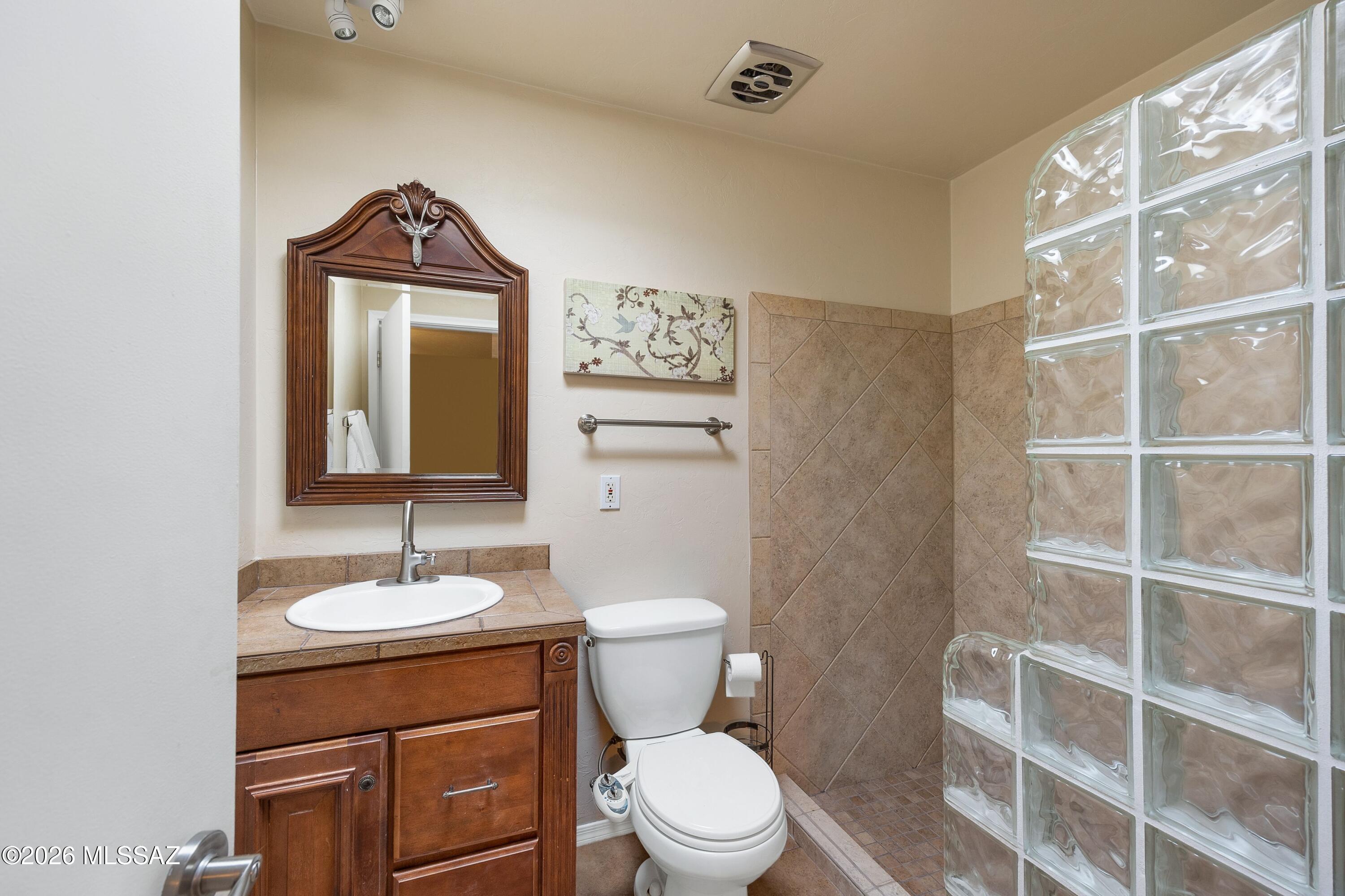 Bathroom with a wood vanity, tan tiled shower, and glass-block partition.