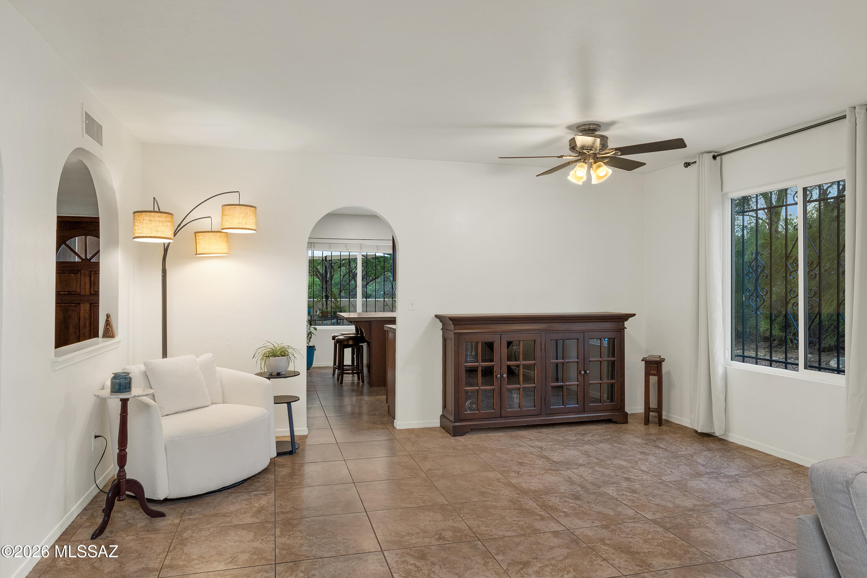 Living room with a white loveseat, dark wood cabinet, tiled floor, and arched openings.
