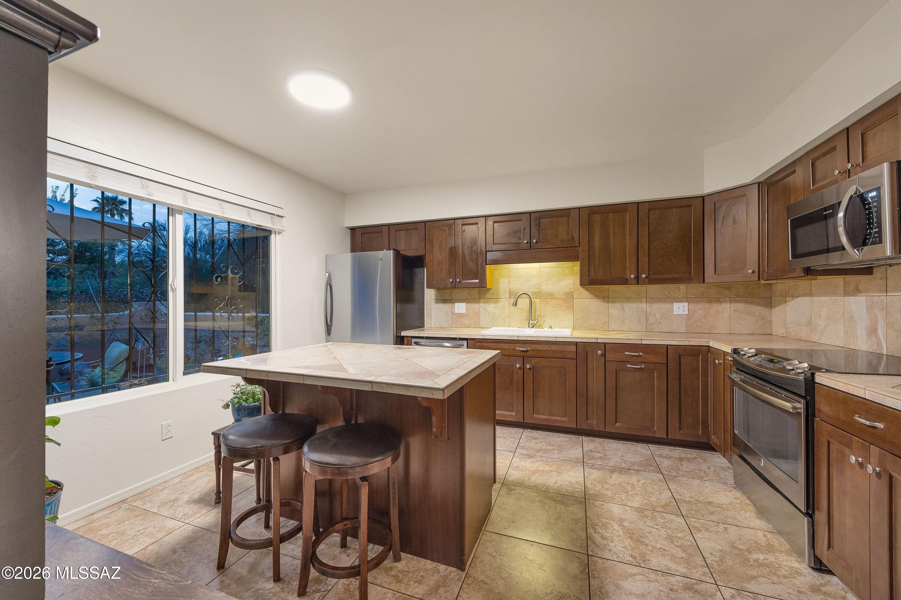 Kitchen with dark wood cabinets, stainless steel appliances, and a tiled island with two stools.