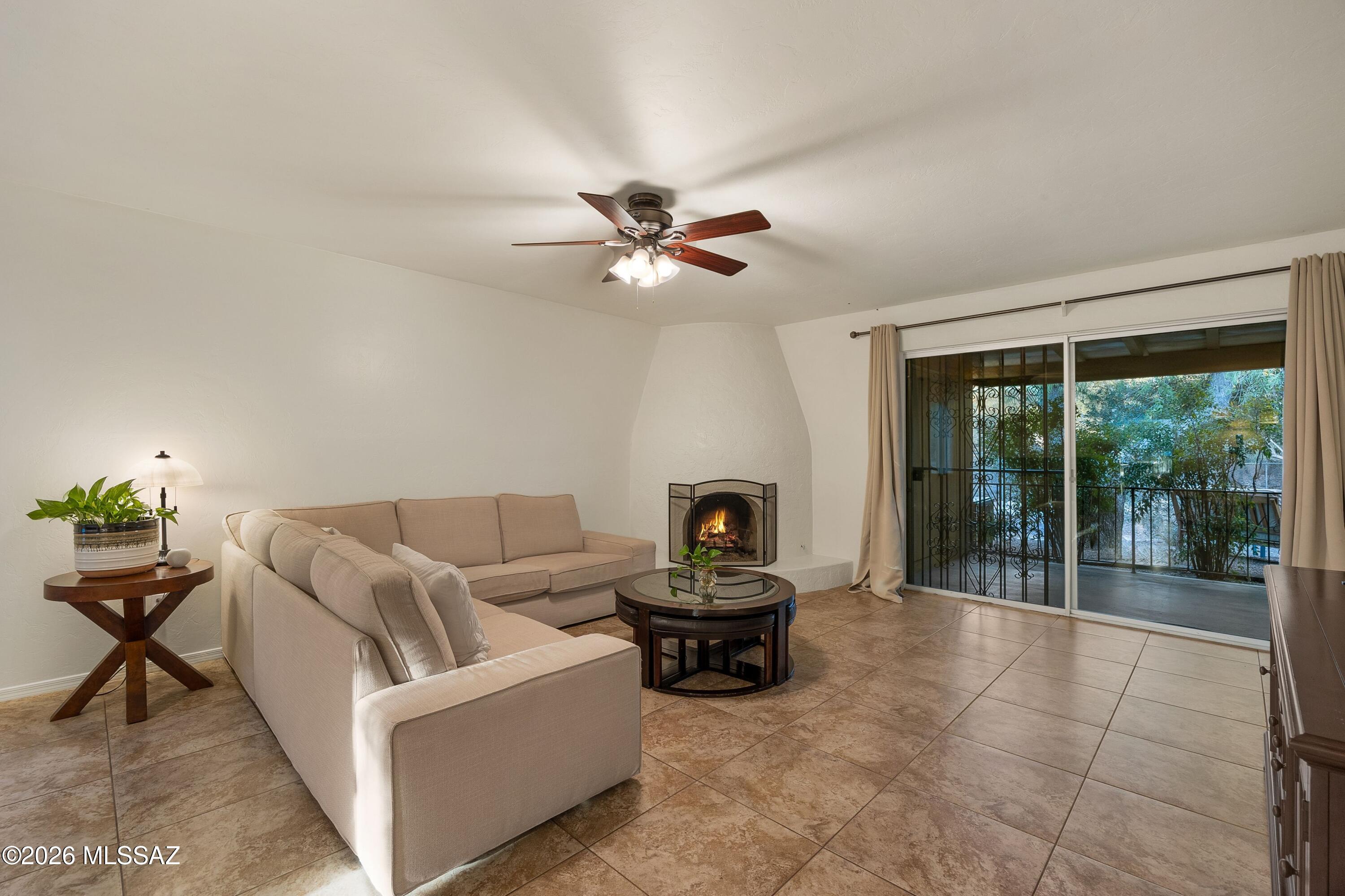 Living room with beige sofas, a lit fireplace, and sliding glass doors to a leafy patio.