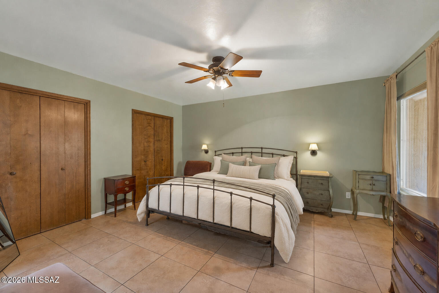 Bedroom with a metal bed, wood closet doors, tiled floors, and a ceiling fan.