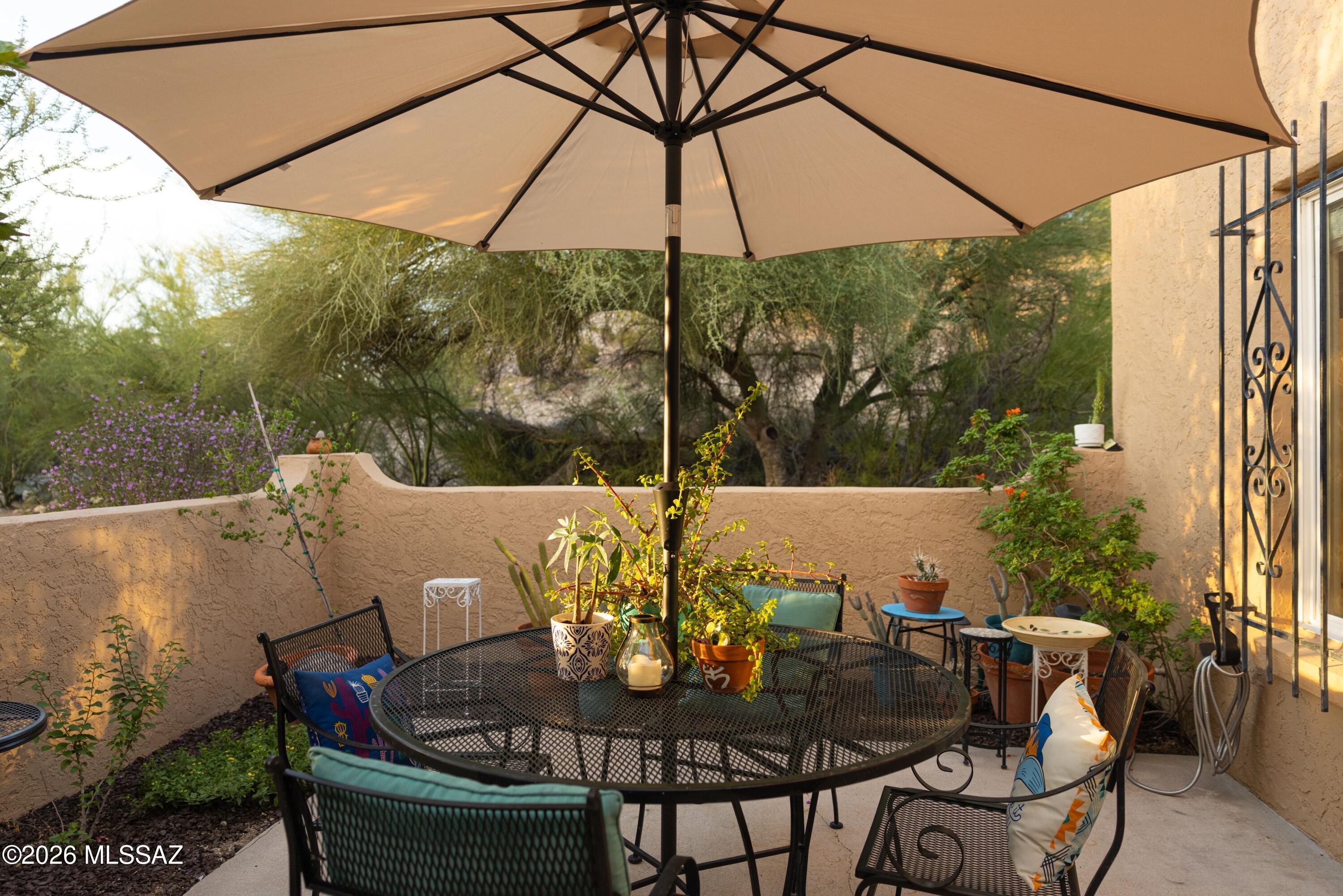 Furnished patio with a large shade umbrella, metal dining set, and potted plants.