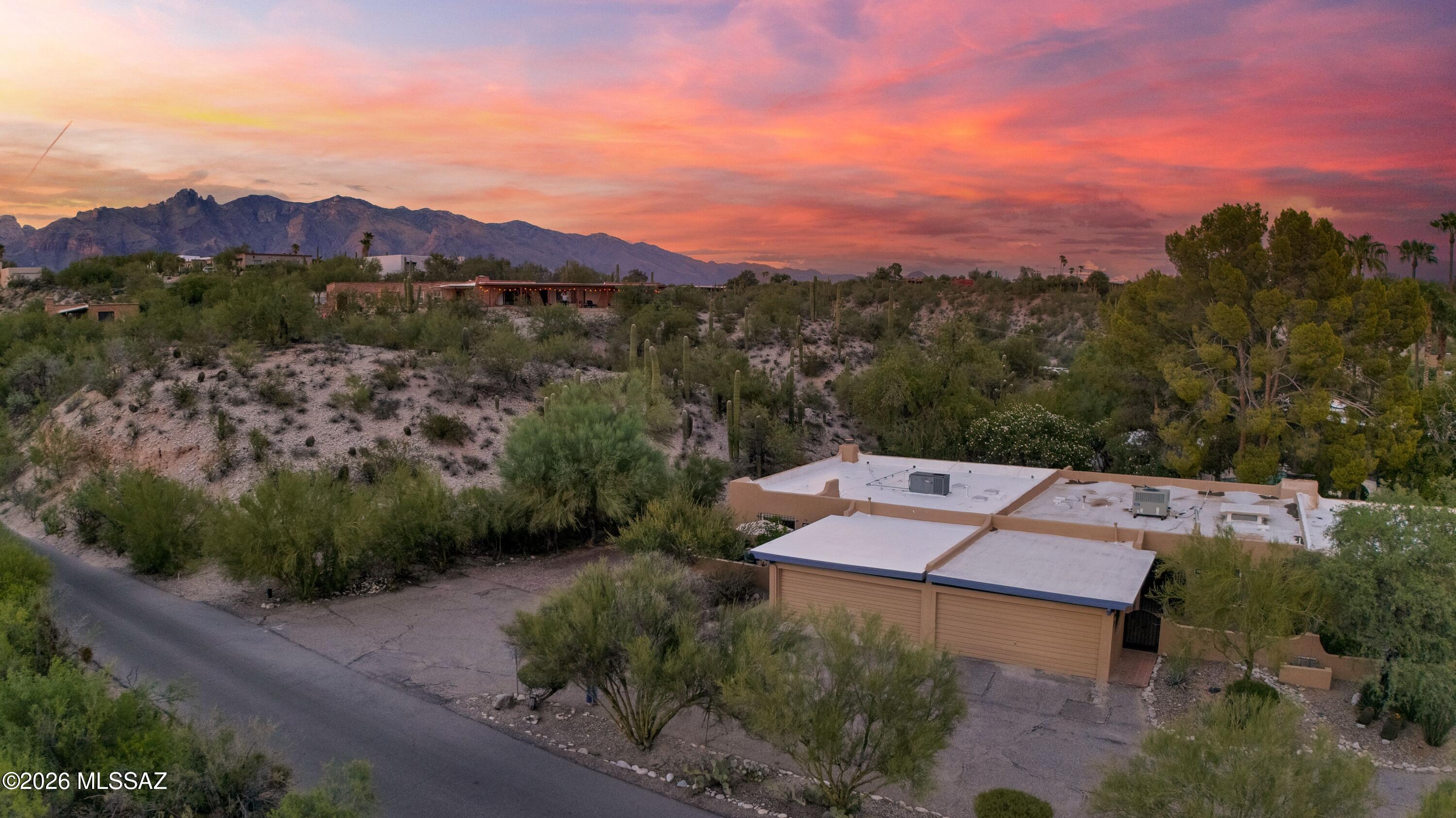 Desert home with flat roof, surrounded by cacti, beneath Tucson mountain ridges at dusk.