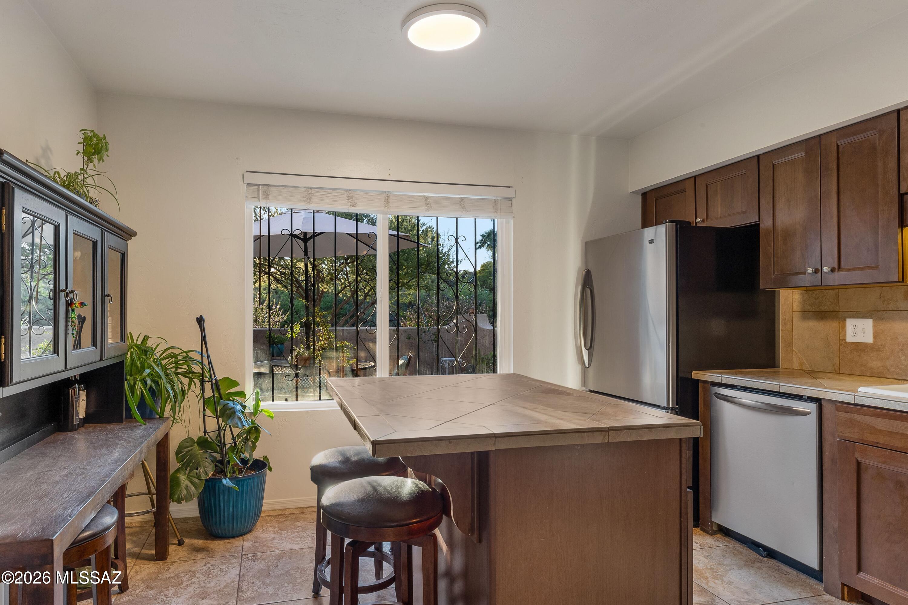 Kitchen with a tiled island, dark wood cabinets, stainless steel appliances, and a window overlooking a leafy patio.