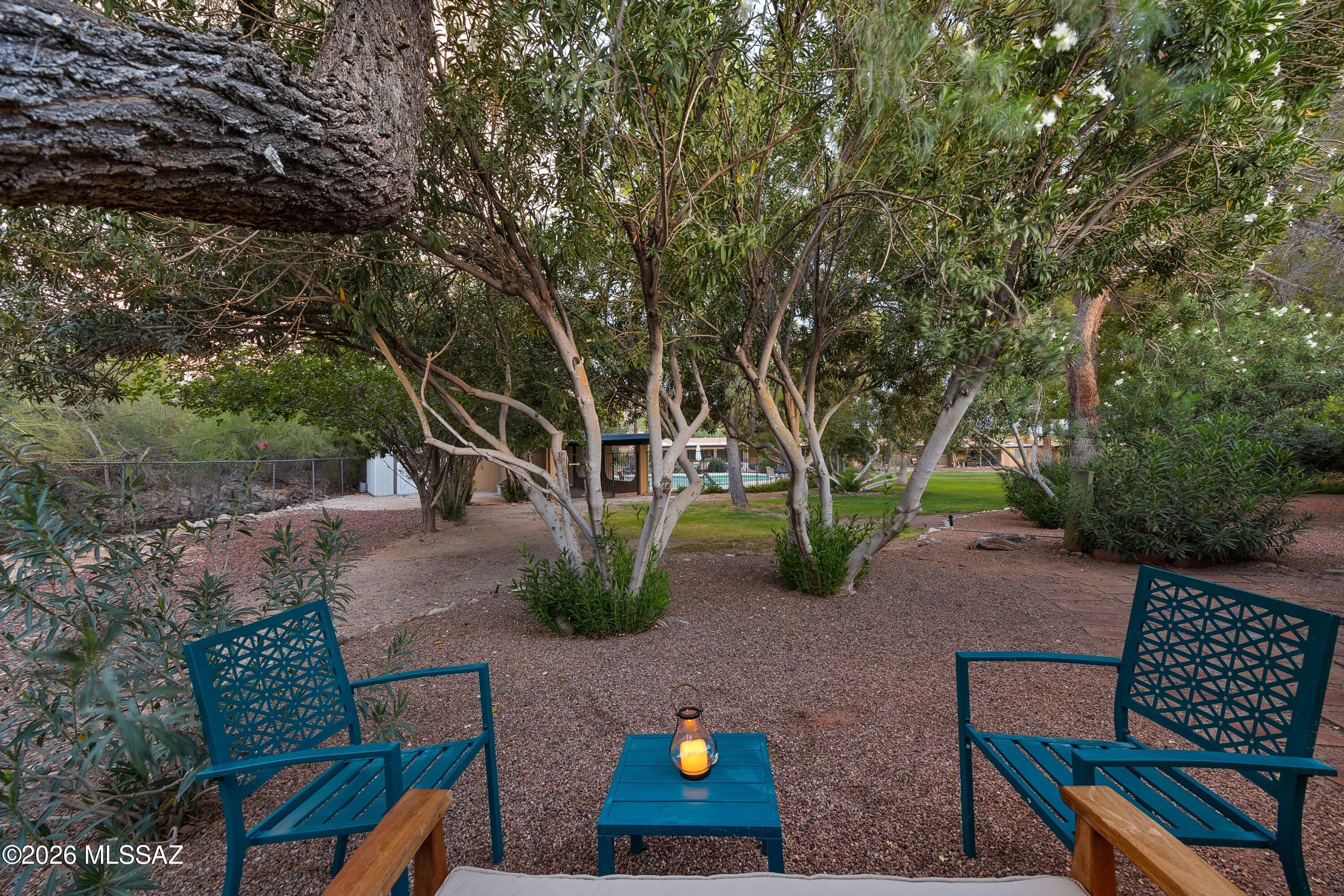 Shaded gravel patio with teal chairs and a table beneath mature trees.