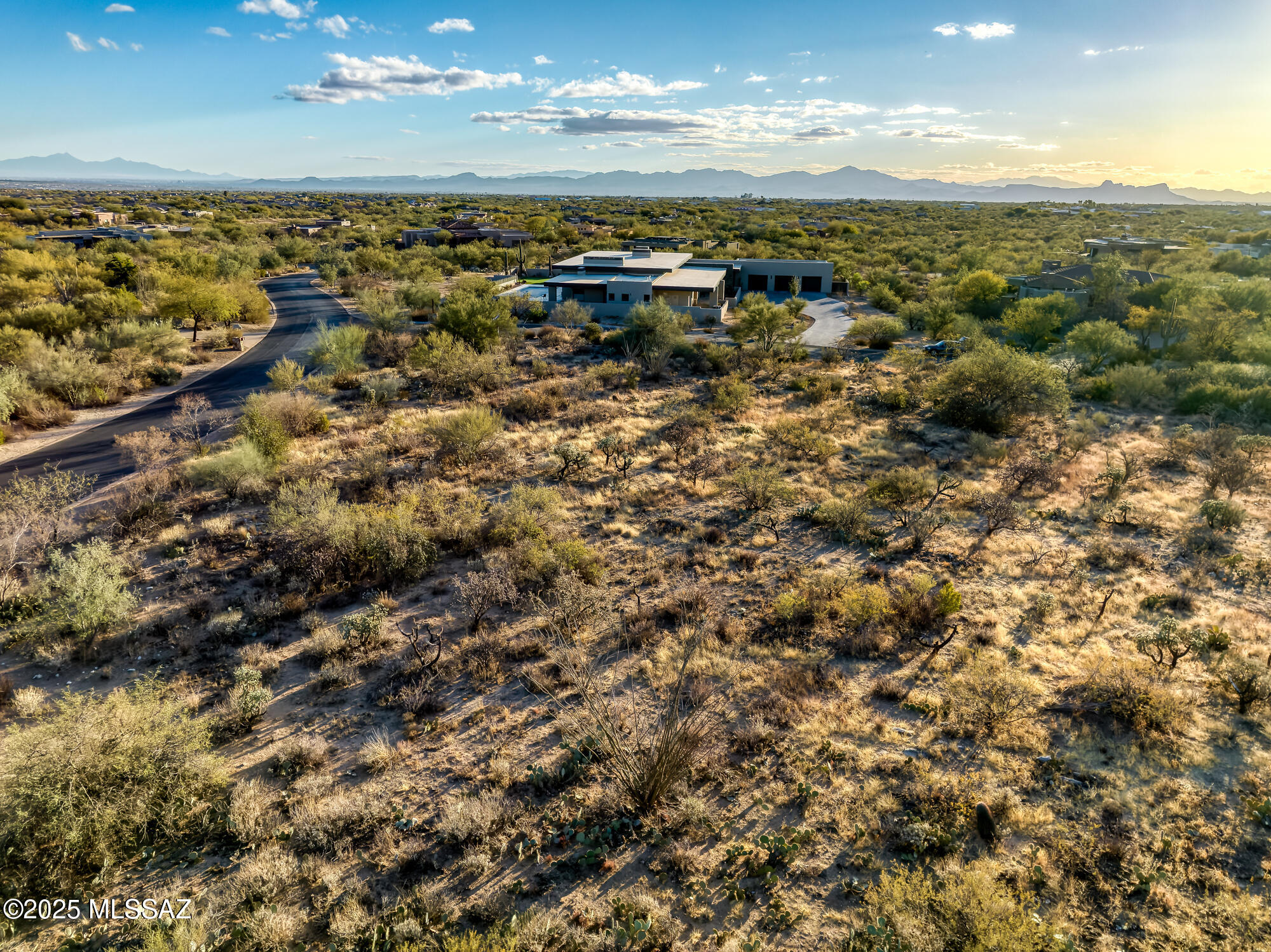 Aerial view of a modern desert home amid Sonoran vegetation, with distant mountains.