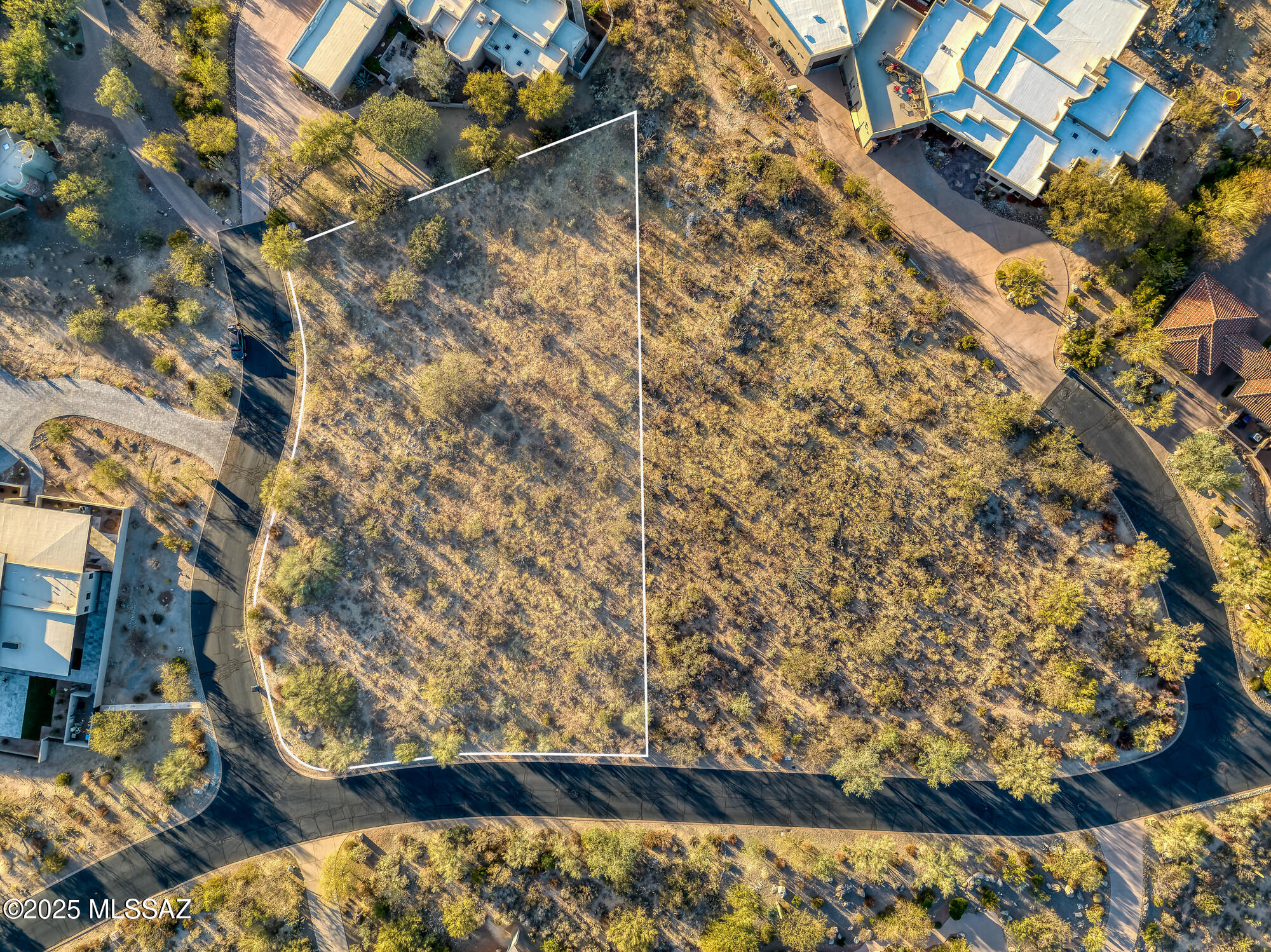 Aerial view of a vacant desert lot outlined in white among homes and curving neighborhood streets.