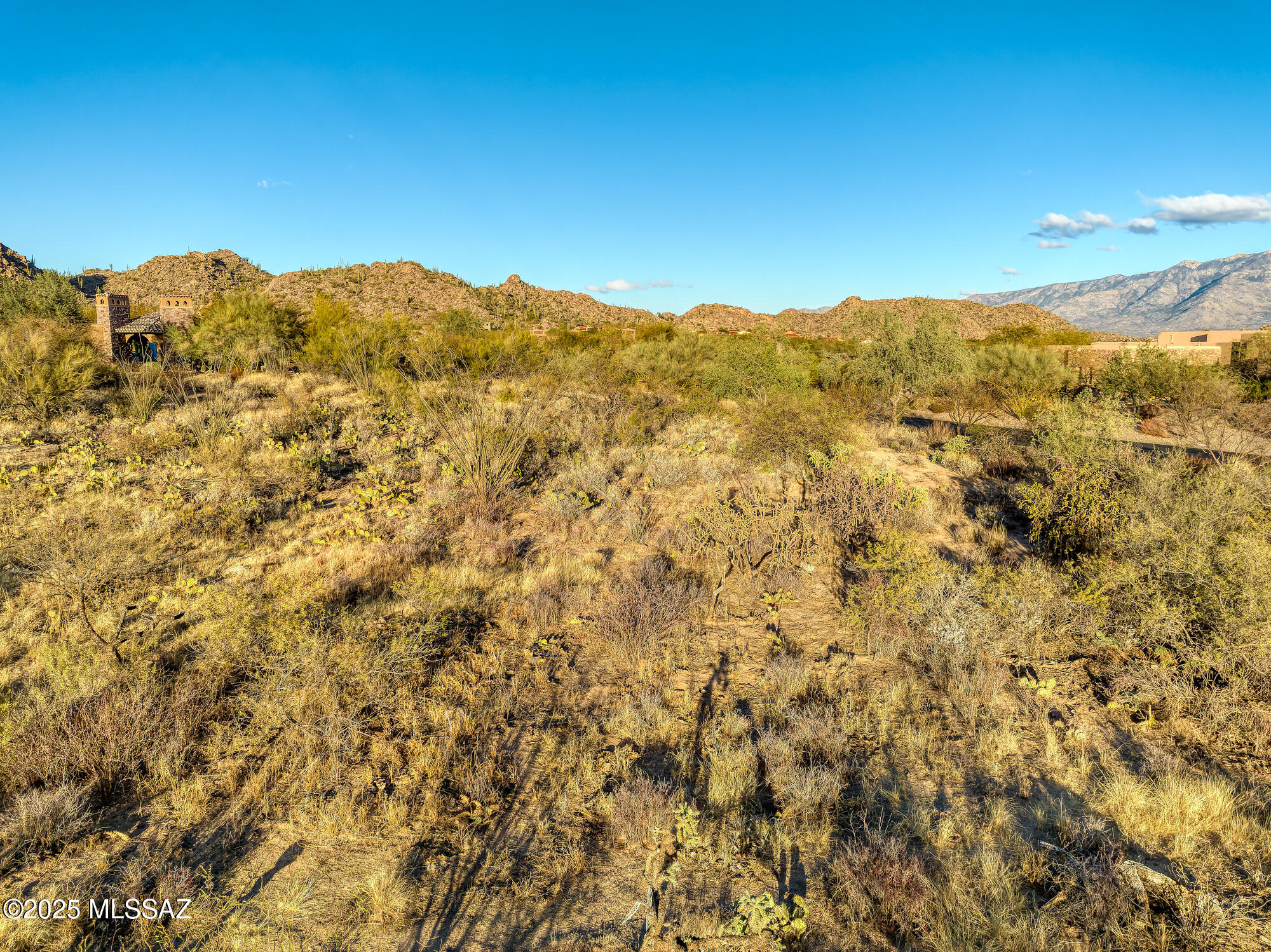 Desert property with native scrub and rocky mountain views beneath a clear blue sky.