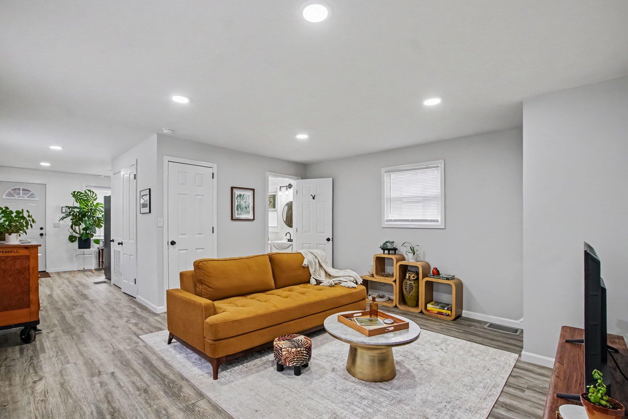 Living room with a mustard-brown sofa, round coffee table, and gray wood-look flooring.