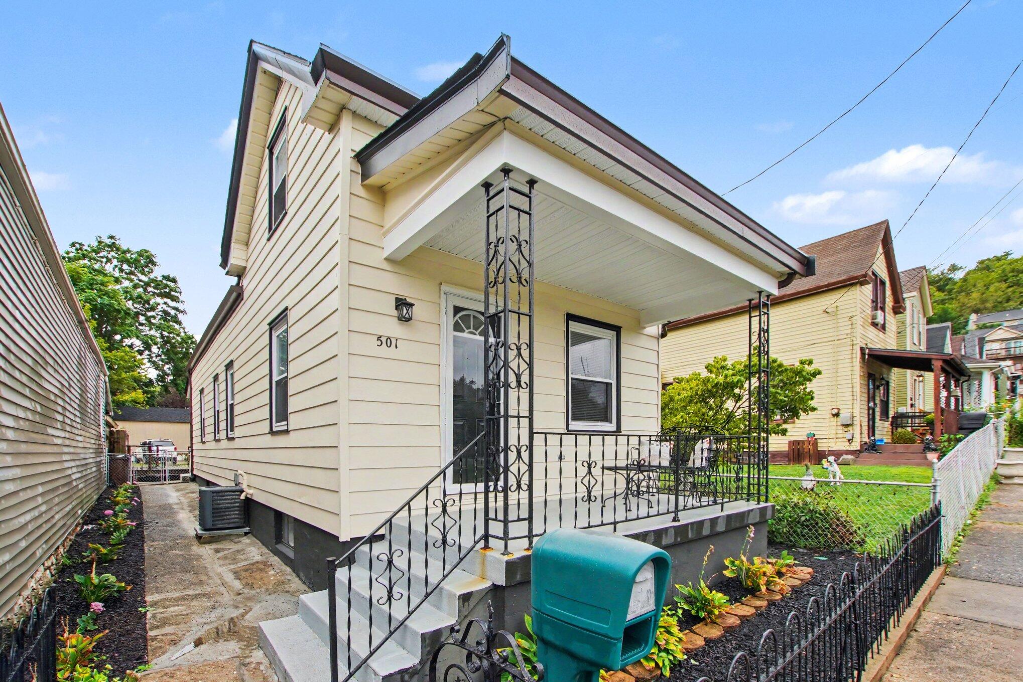 Cream-sided home with a covered porch, decorative iron railings, and landscaped front walk.