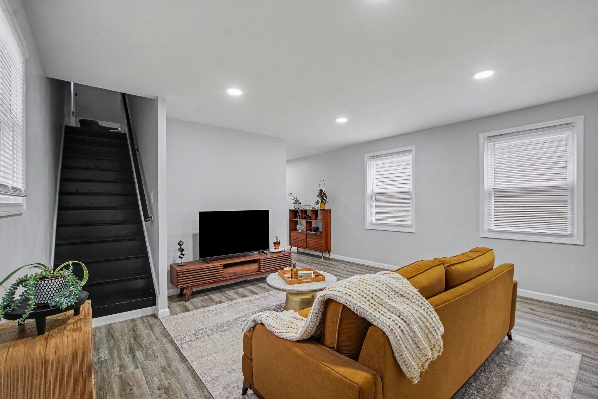 Living room with a mustard sofa, dark staircase, and wooden media console.