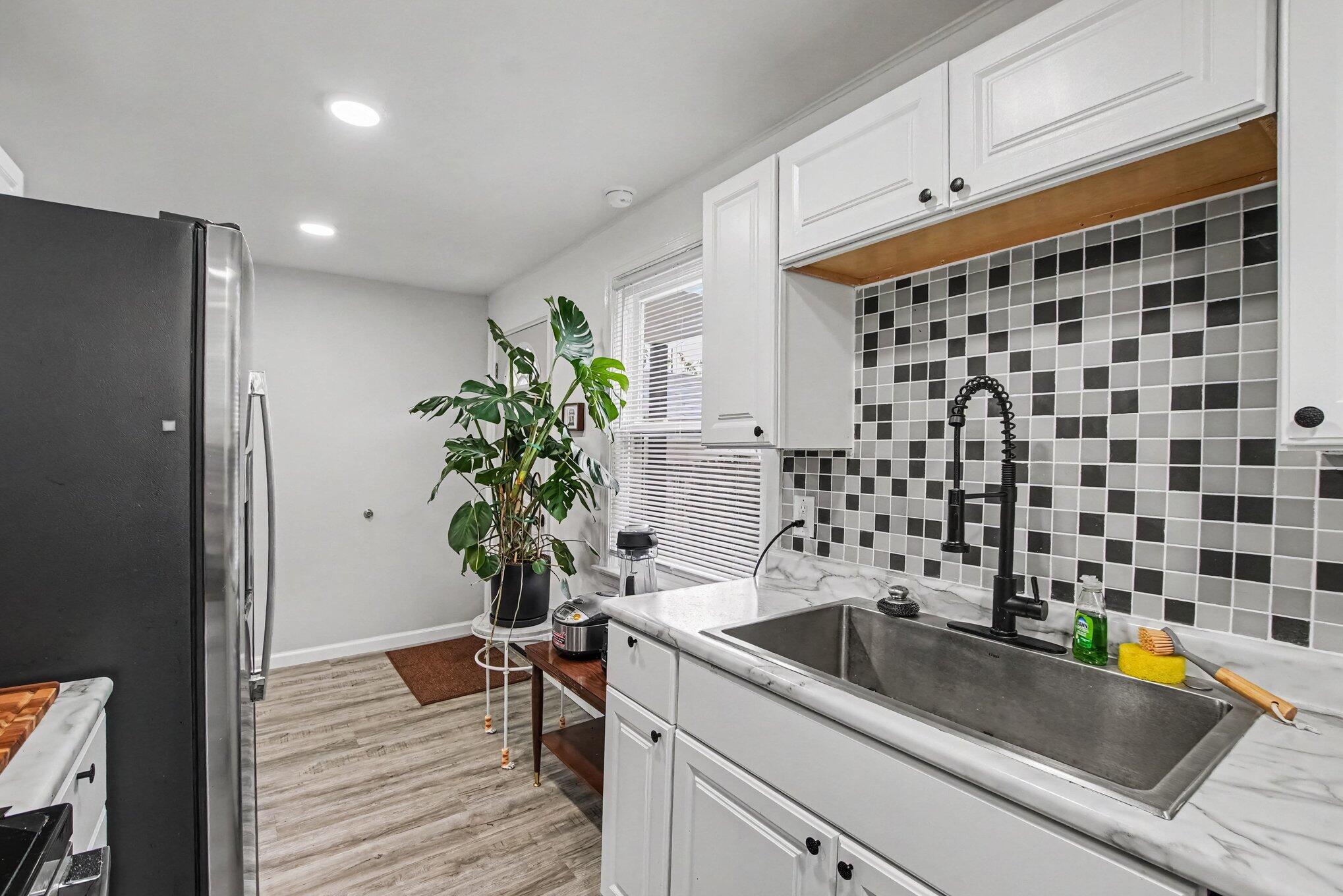 Kitchen with checkerboard tile backsplash, white cabinetry, and a large stainless sink with black faucet.