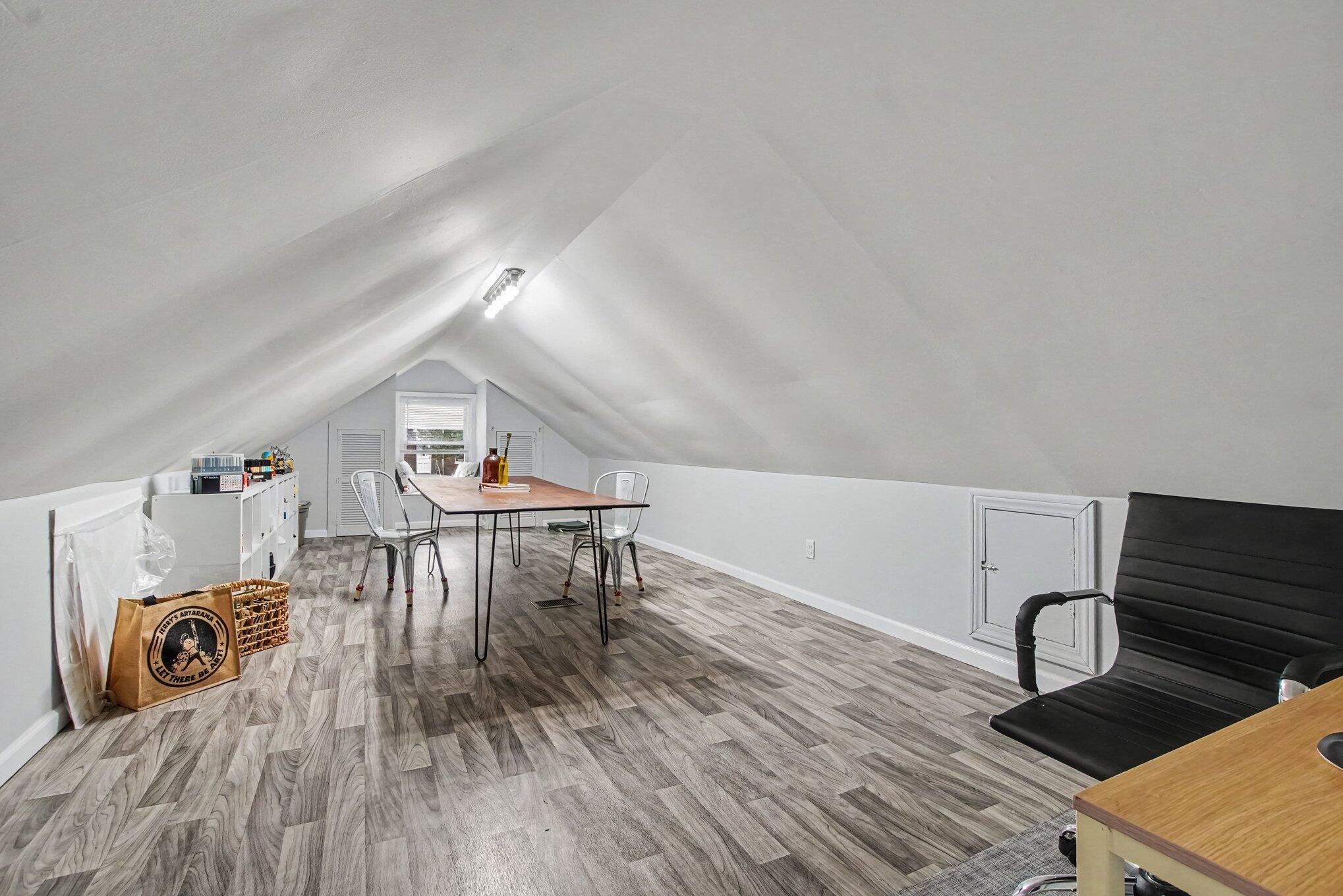 Finished attic with sloped ceiling, gray wood-look floors, a table, and metal chairs.