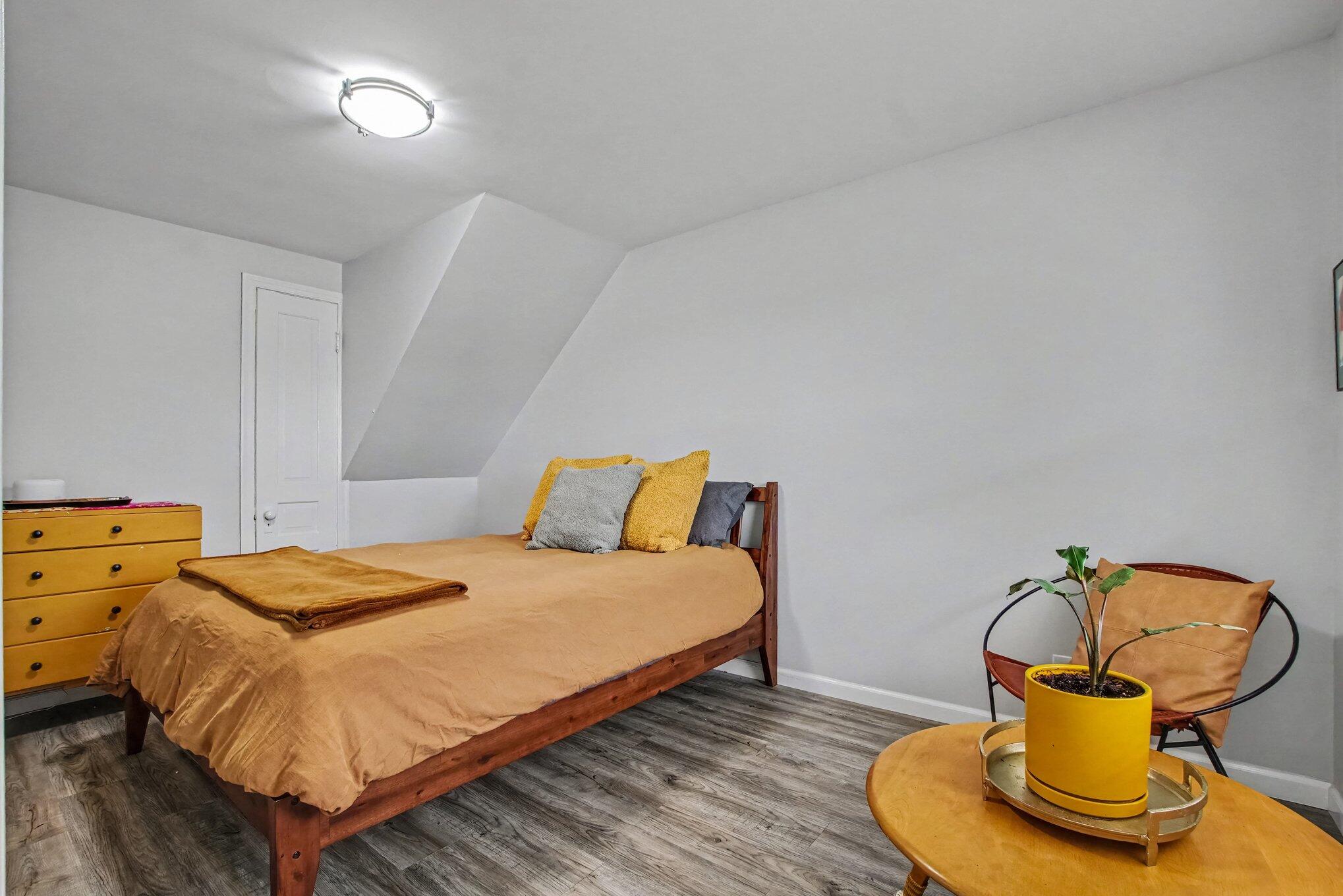 Bedroom with mustard bedding, a sloped ceiling, and a potted plant beside a chair.