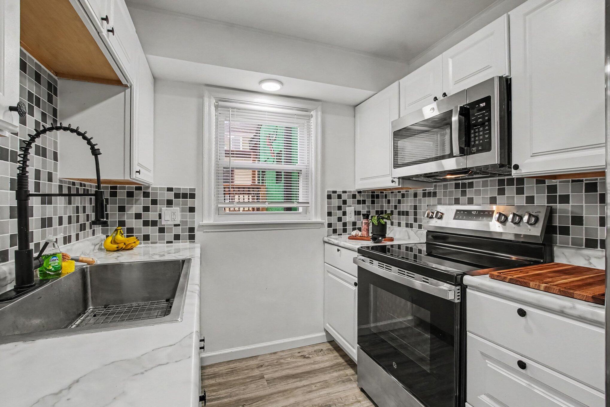 Kitchen with white cabinets, checkerboard tile backsplash, deep sink, and stainless steel appliances.