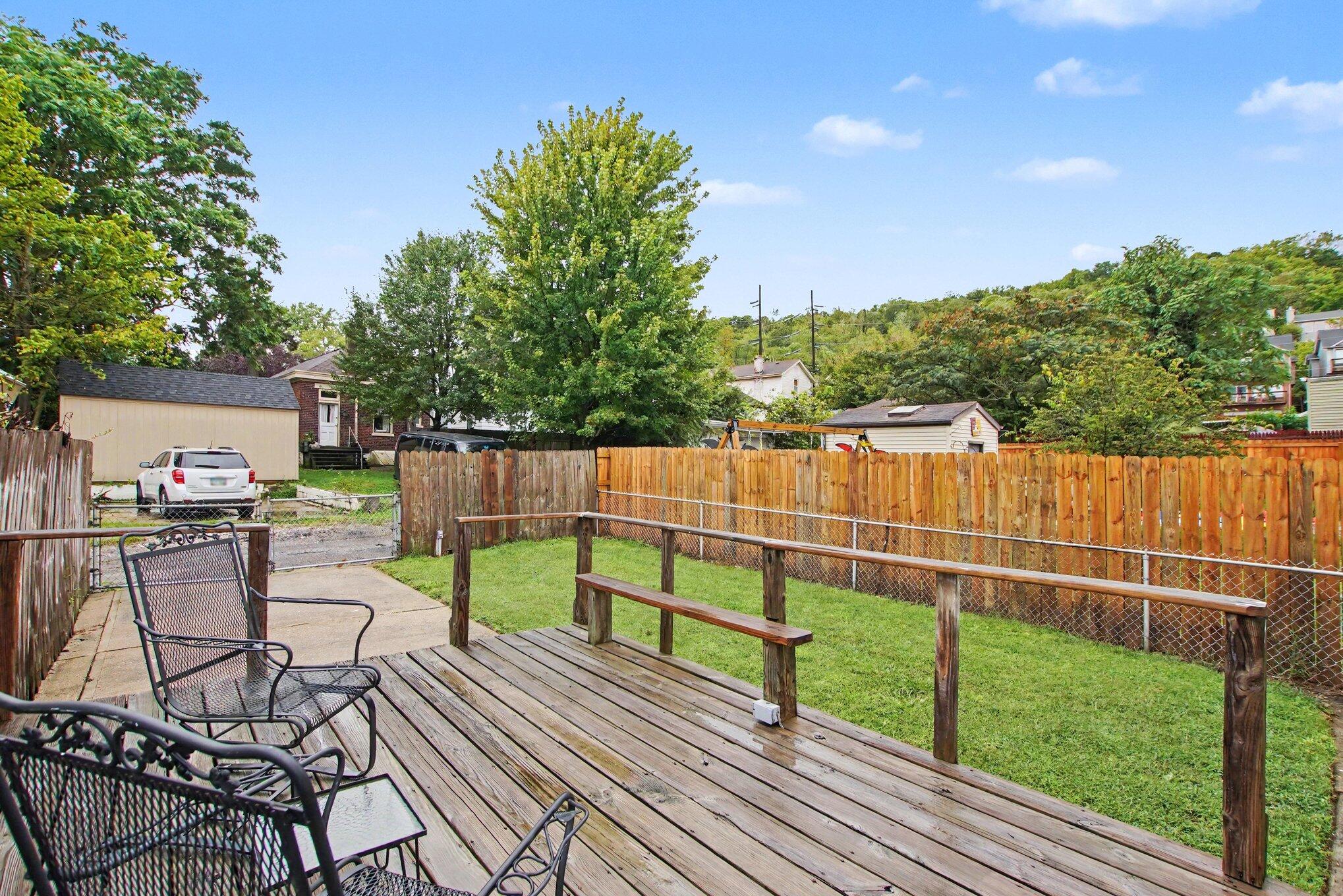 Fenced backyard with a wooden deck, black patio chairs, and a small lawn.