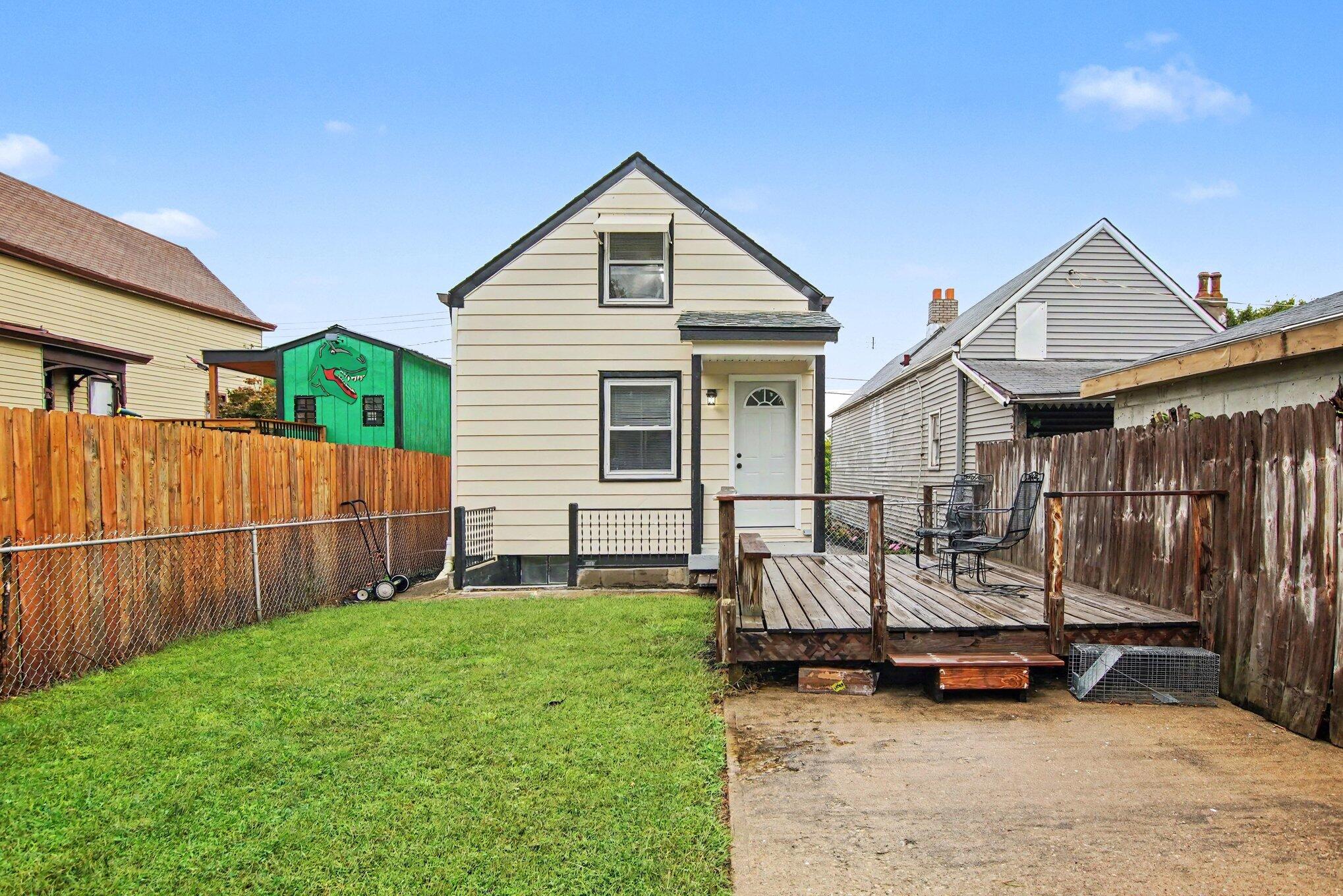 Rear of a cream-sided house with a wooden deck, fenced lawn, and neighboring homes.