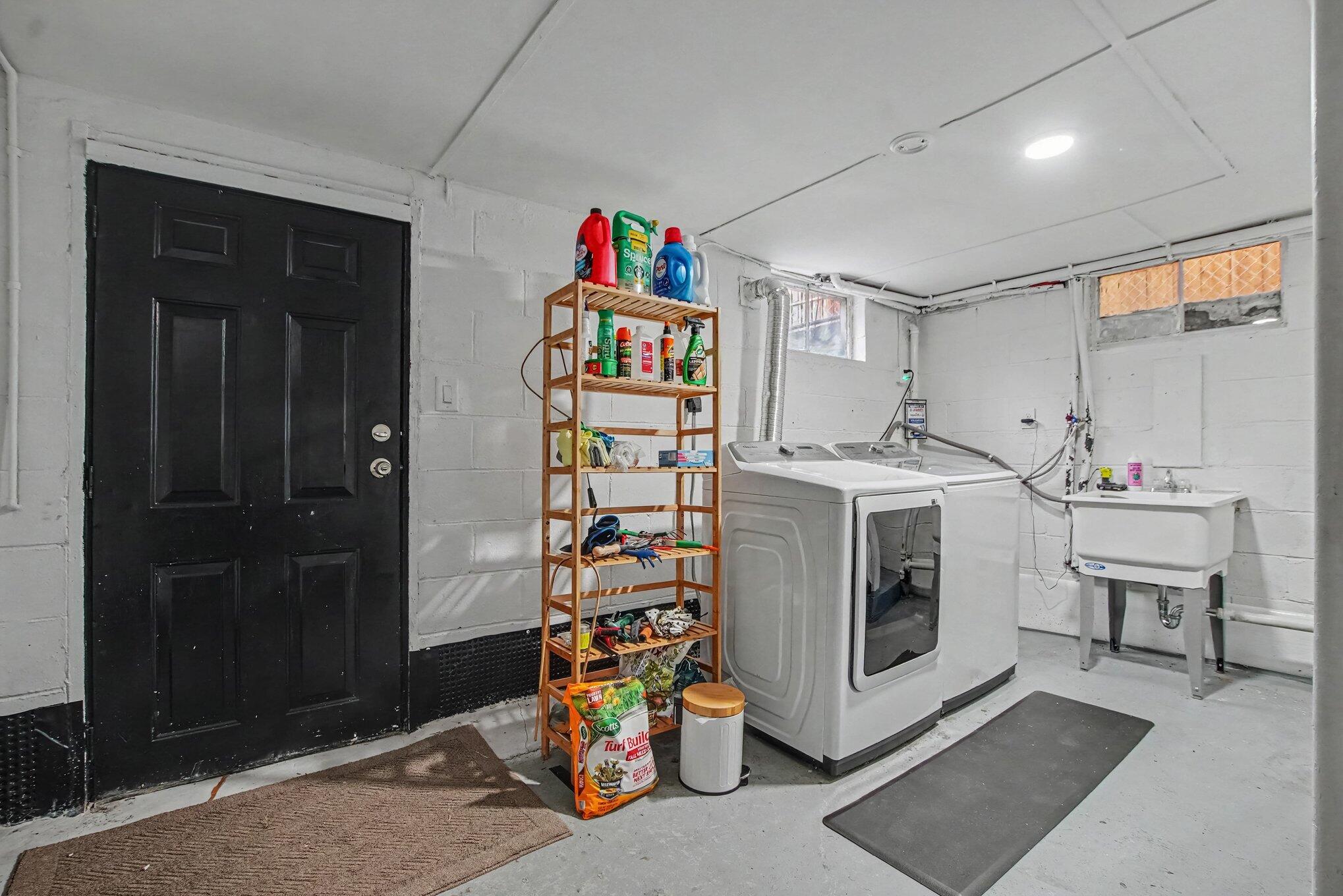 Basement laundry room with washer, dryer, utility sink, and a stocked wooden storage shelf.