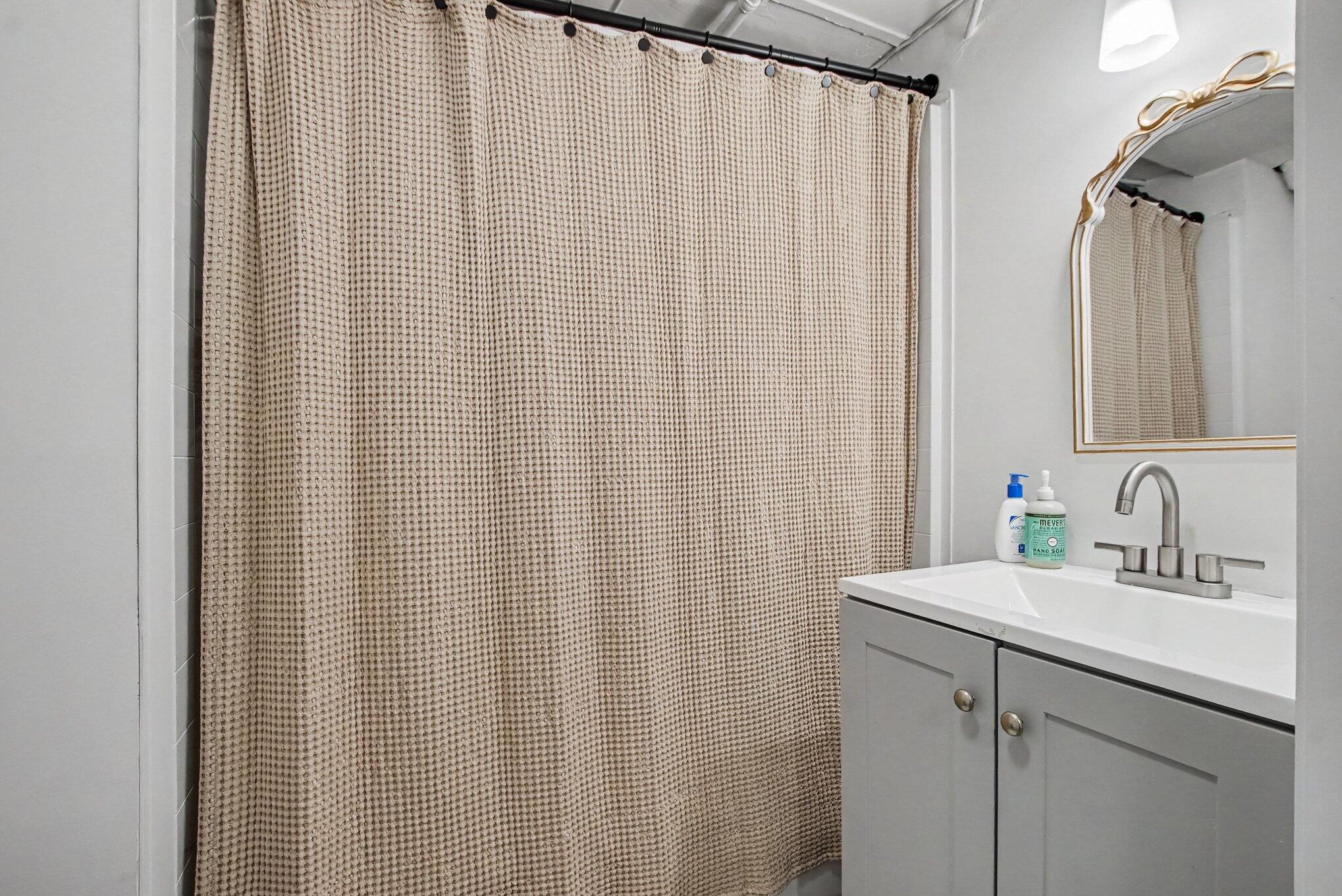 Bathroom vanity with a gold-framed mirror beside a beige textured shower curtain.