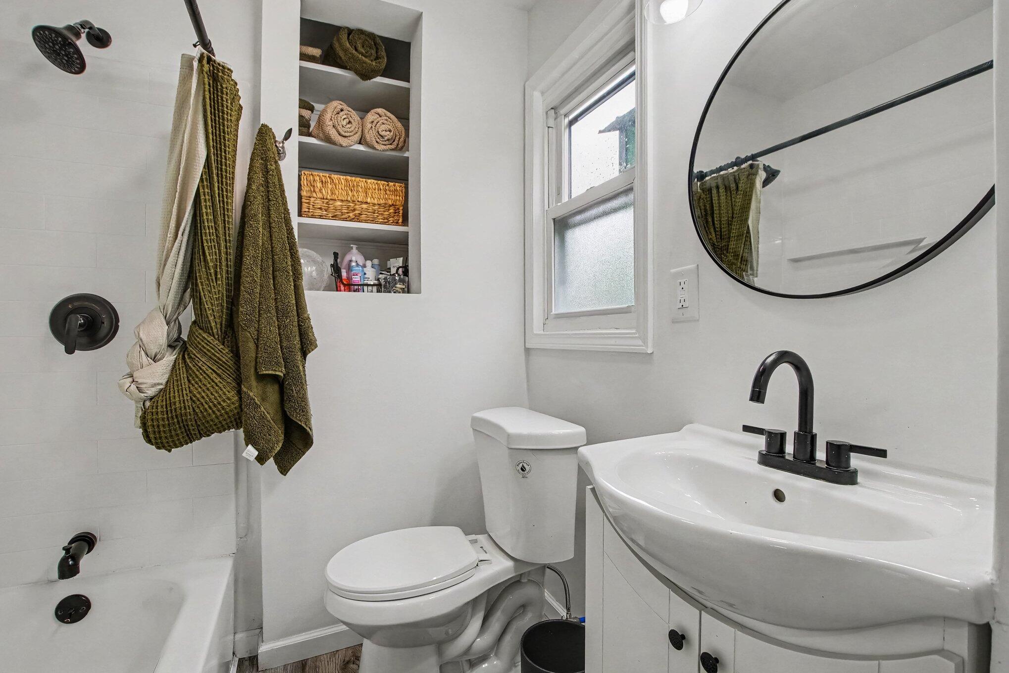 Bathroom with a tub-shower, white sink, black fixtures, and recessed towel shelves.