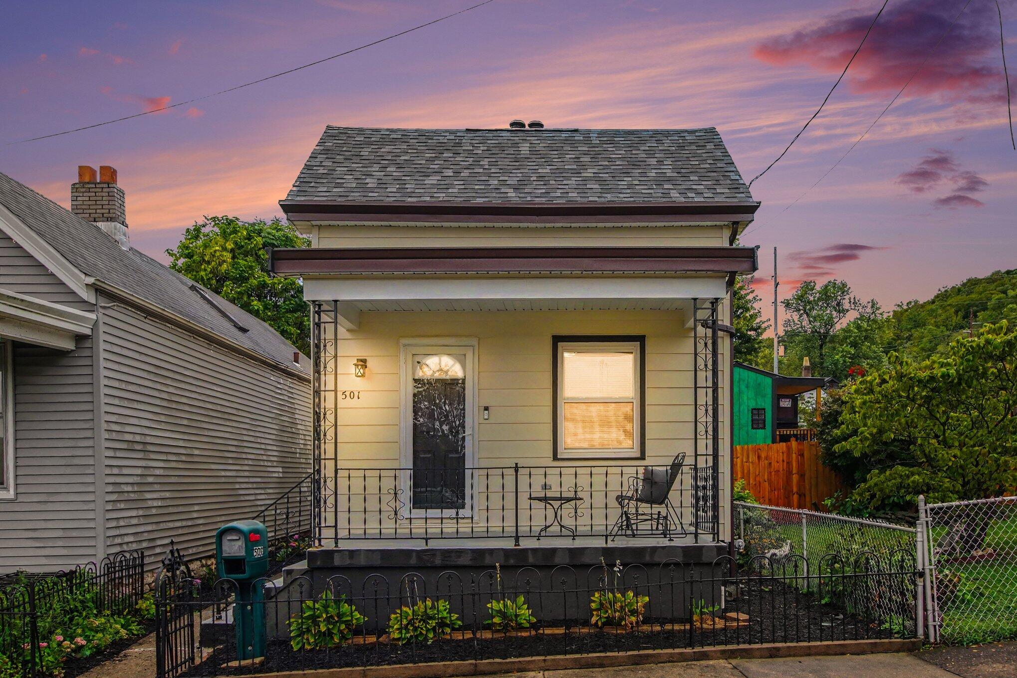 Small cream house with a covered porch and black iron railings at dusk.