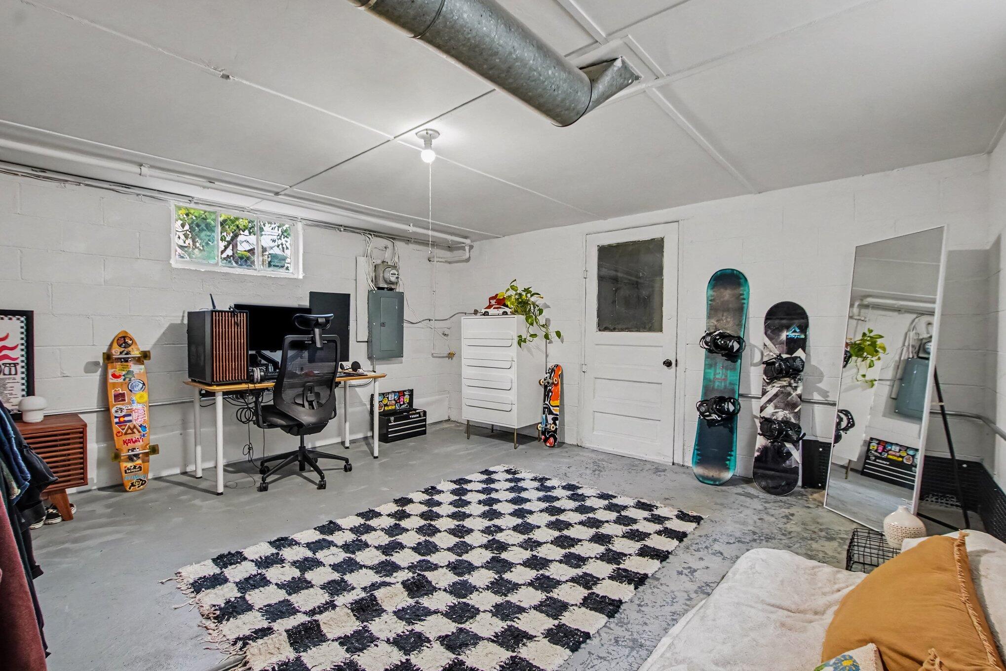Furnished basement room with a desk, checkered rug, and snowboards displayed along the wall.