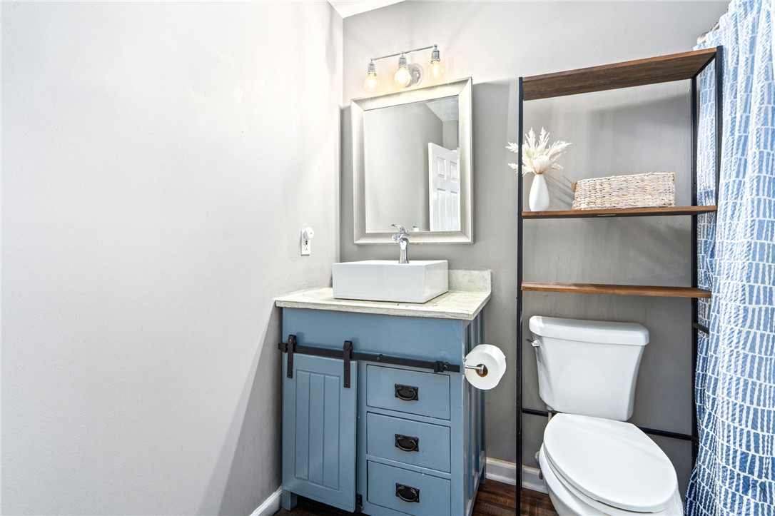 Bathroom with a blue vanity, vessel sink, toilet, and open shelving beside a patterned shower curtain.