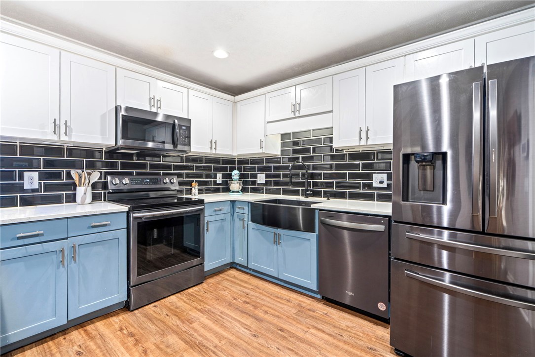 Kitchen with blue cabinets, black tile backsplash, and stainless steel appliances.