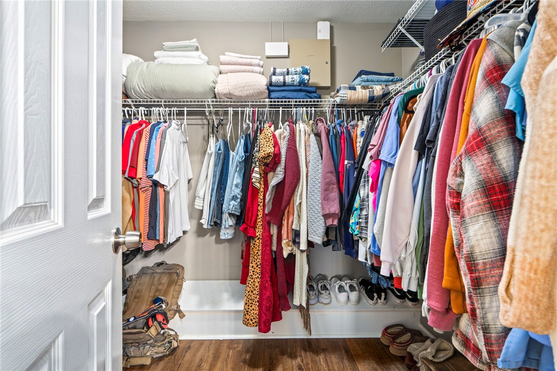 Walk-in closet with clothes on racks, folded linens on shelves, and shoes below.