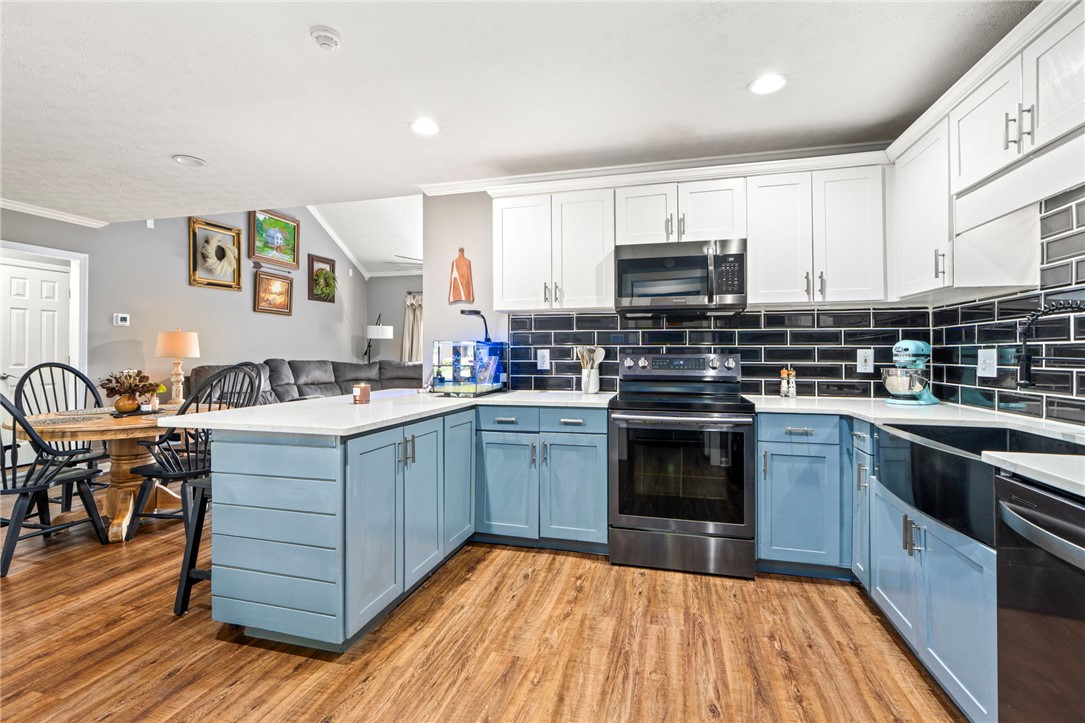 Kitchen with blue cabinets, black tile backsplash, white counters, and stainless steel appliances.