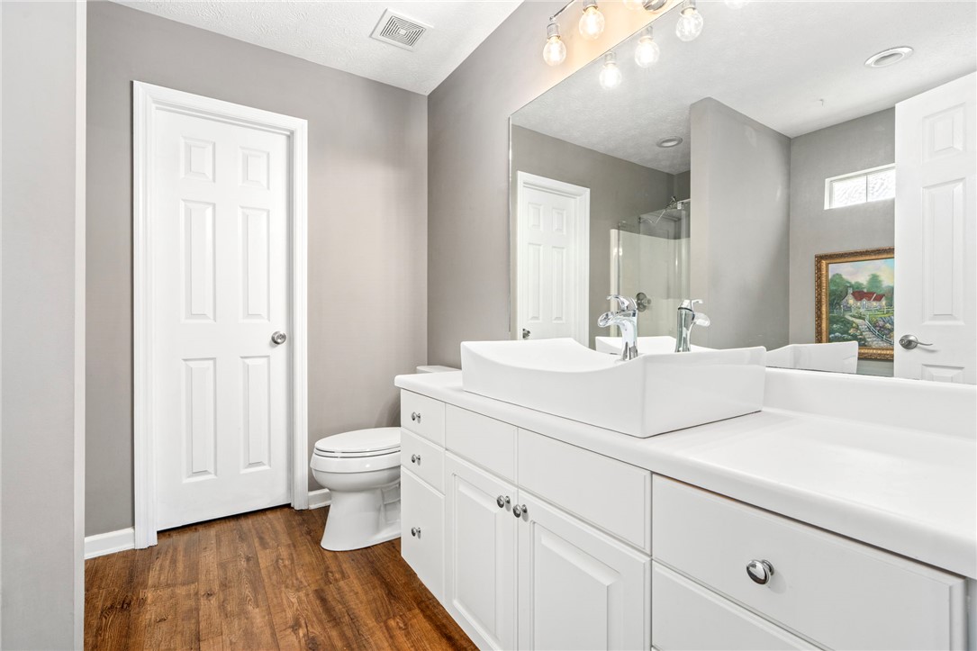 Bathroom with a white double vanity, vessel sinks, large mirror, and wood-look flooring.