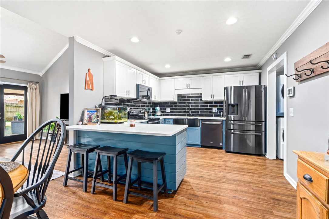 Kitchen with blue island, white cabinets, black tile backsplash, and stainless steel appliances.