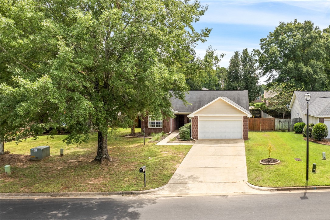 Single-story brick home with an attached garage, wide driveway, and mature shade trees.