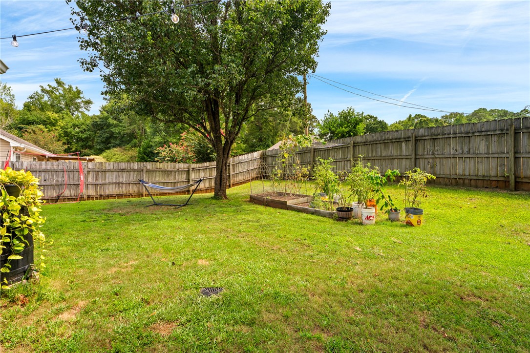 Fenced backyard with a shade tree, hammock, lawn, and raised vegetable beds.