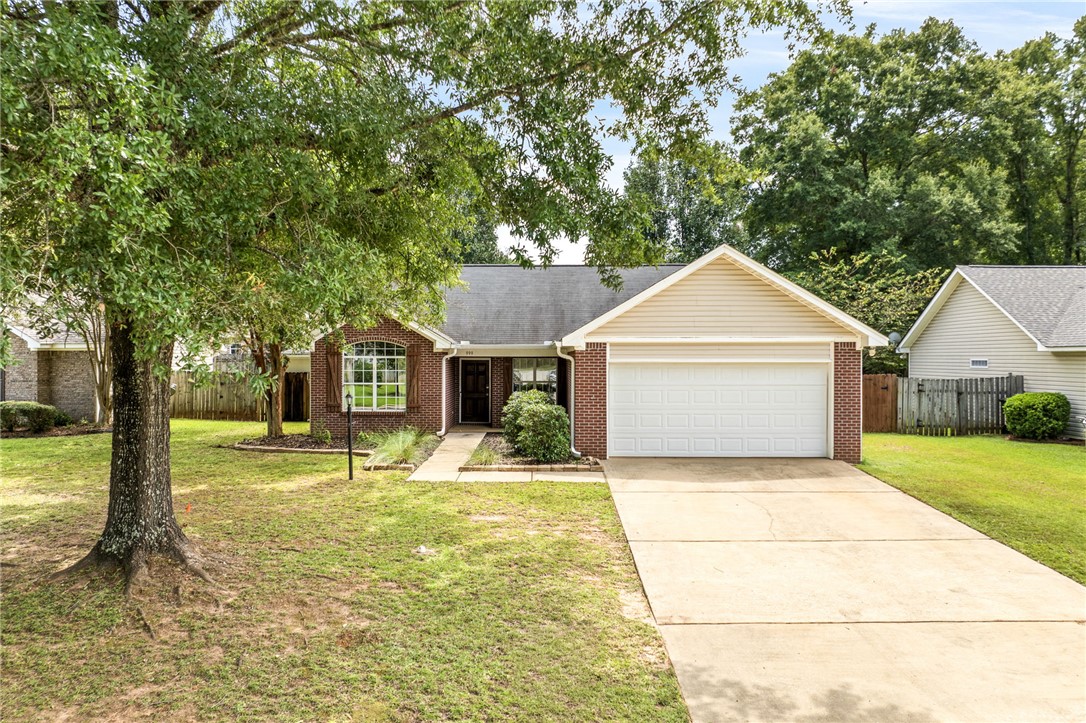 Single-story brick home with an attached garage, wide driveway, and mature trees in the front yard.