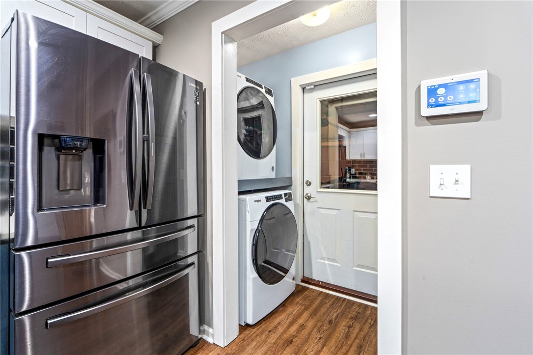Laundry area with stacked washer and dryer beside a stainless-steel refrigerator.