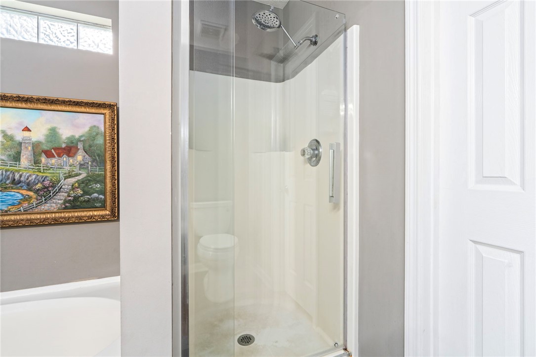 Glass-enclosed shower with chrome fixtures beside a bathtub and framed landscape painting.