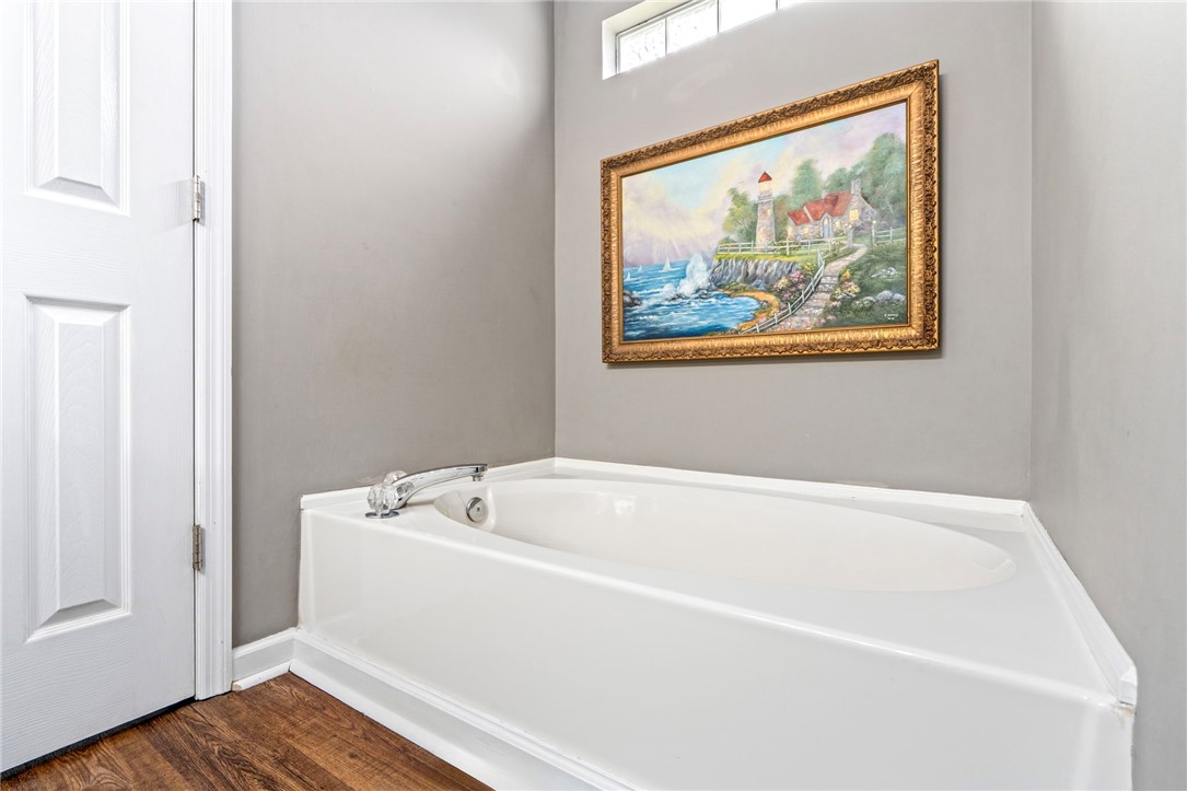 Bathroom with a white bathtub beneath a framed coastal painting.