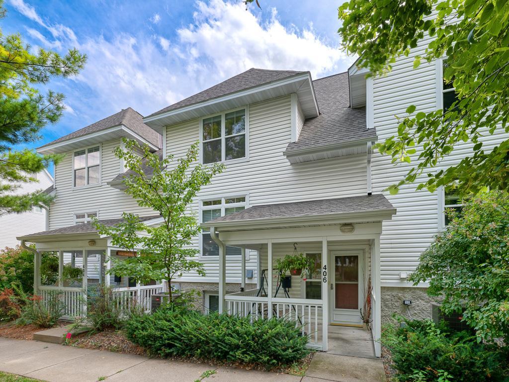White two-story townhouse with covered porches, leafy landscaping, and the number 406 by the entrance.